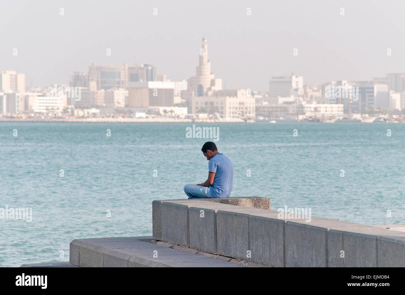 Un uomo si siede da solo a Doha, in Qatar, con il paesaggio e il Golfo Arabico in background. Foto Stock