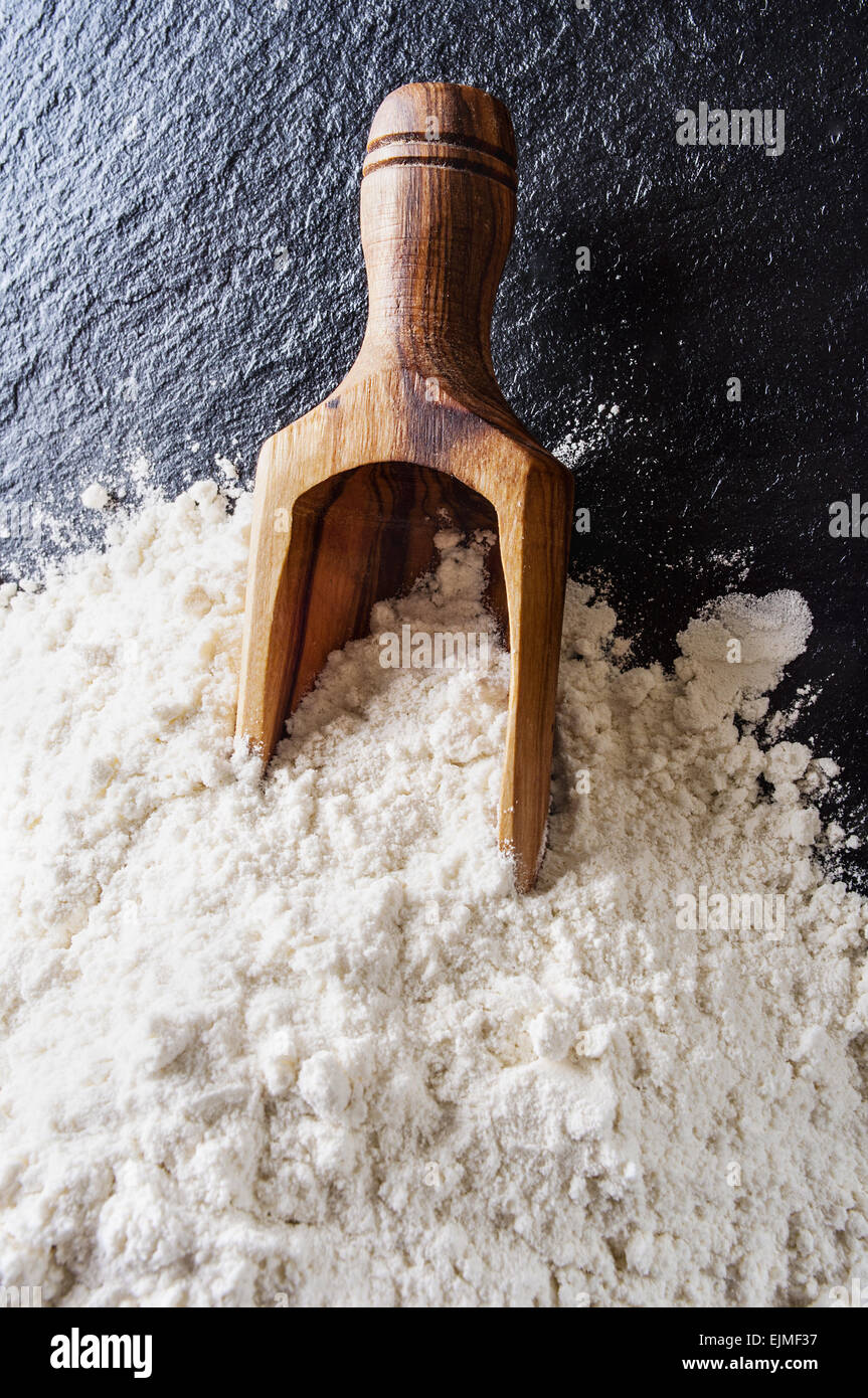 Cucchiaio di legno con la farina sulla tavola nera Foto Stock