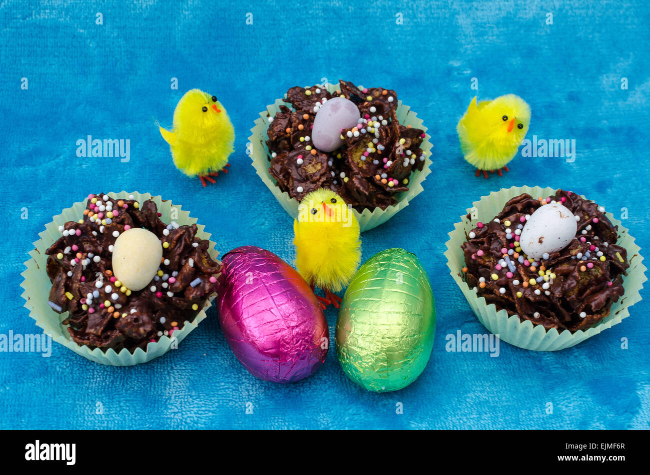 Guardando verso il basso su una perfetta Pasqua raccolta di uova di pasqua di cioccolato, torte di cornflake e piccolo bambino giocattolo giallo pulcini Foto Stock