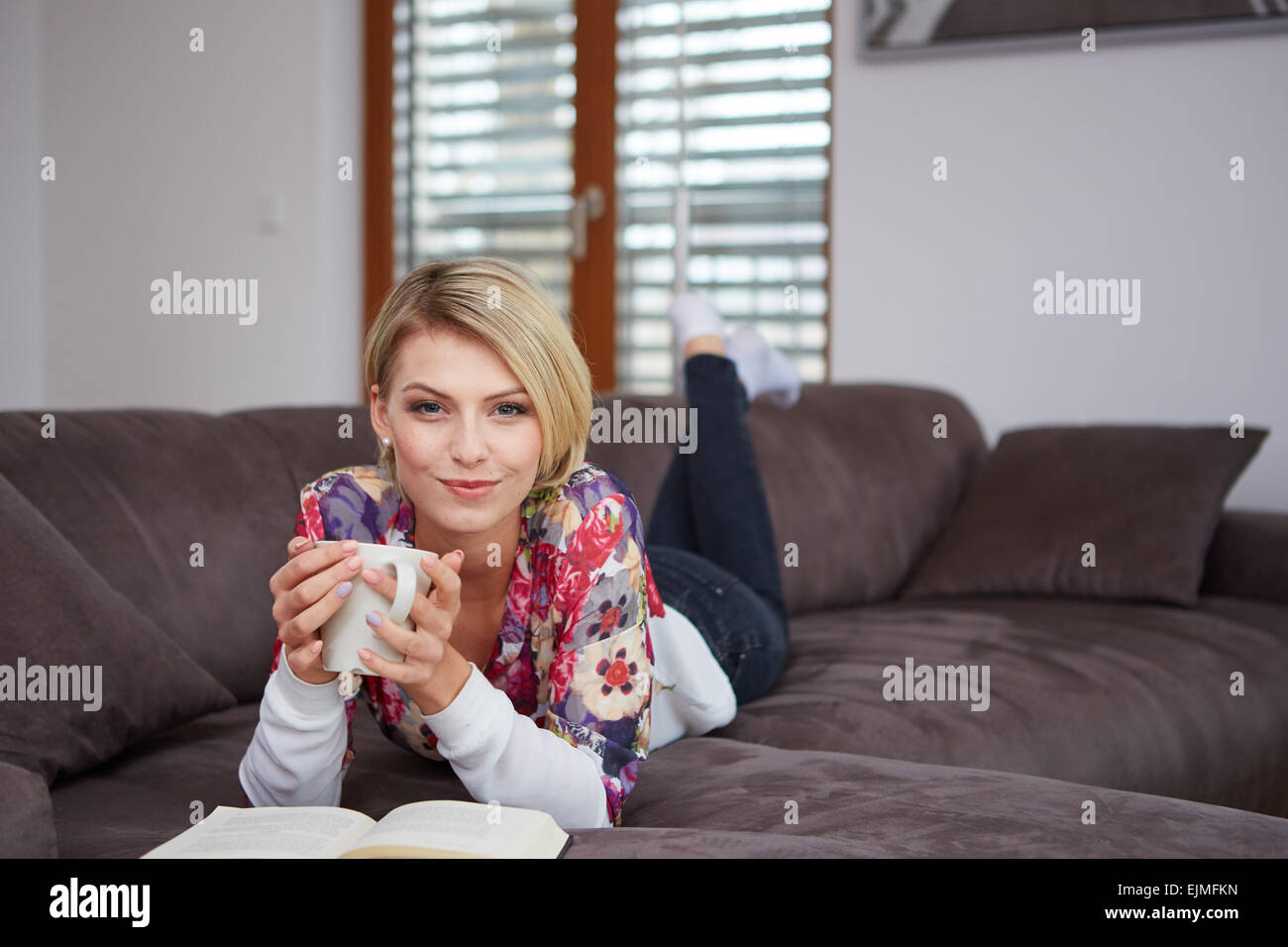 Donna godendo la lettura di un libro a casa sdraiato sul divano Foto Stock