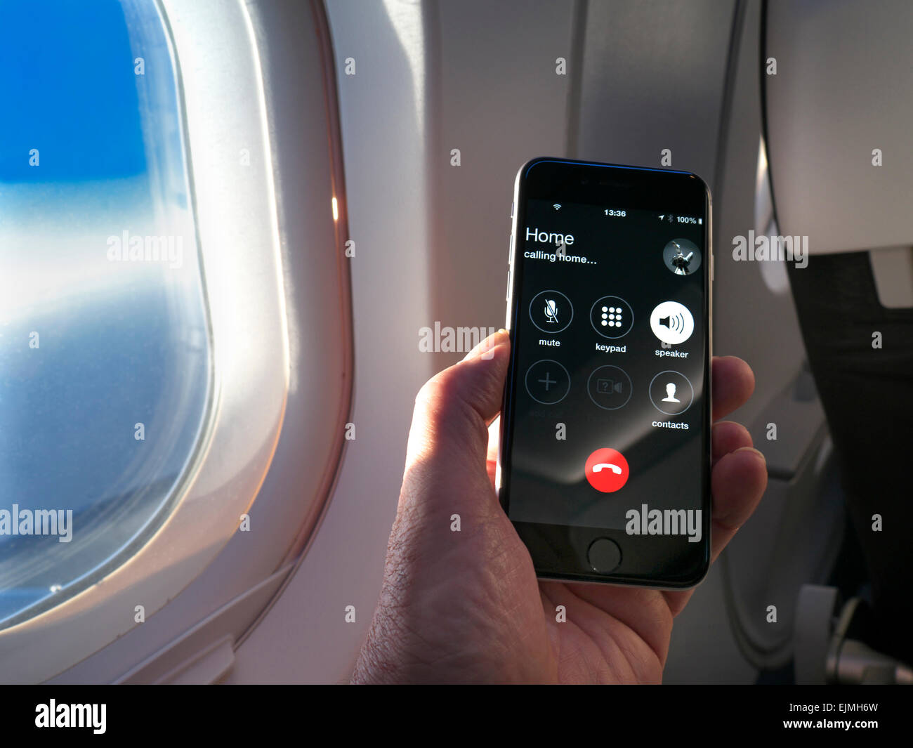 Smartphone iPhone portatile con schermo che chiama "casa" durante il volo, con ala della finestra della cabina e cielo blu dietro Foto Stock