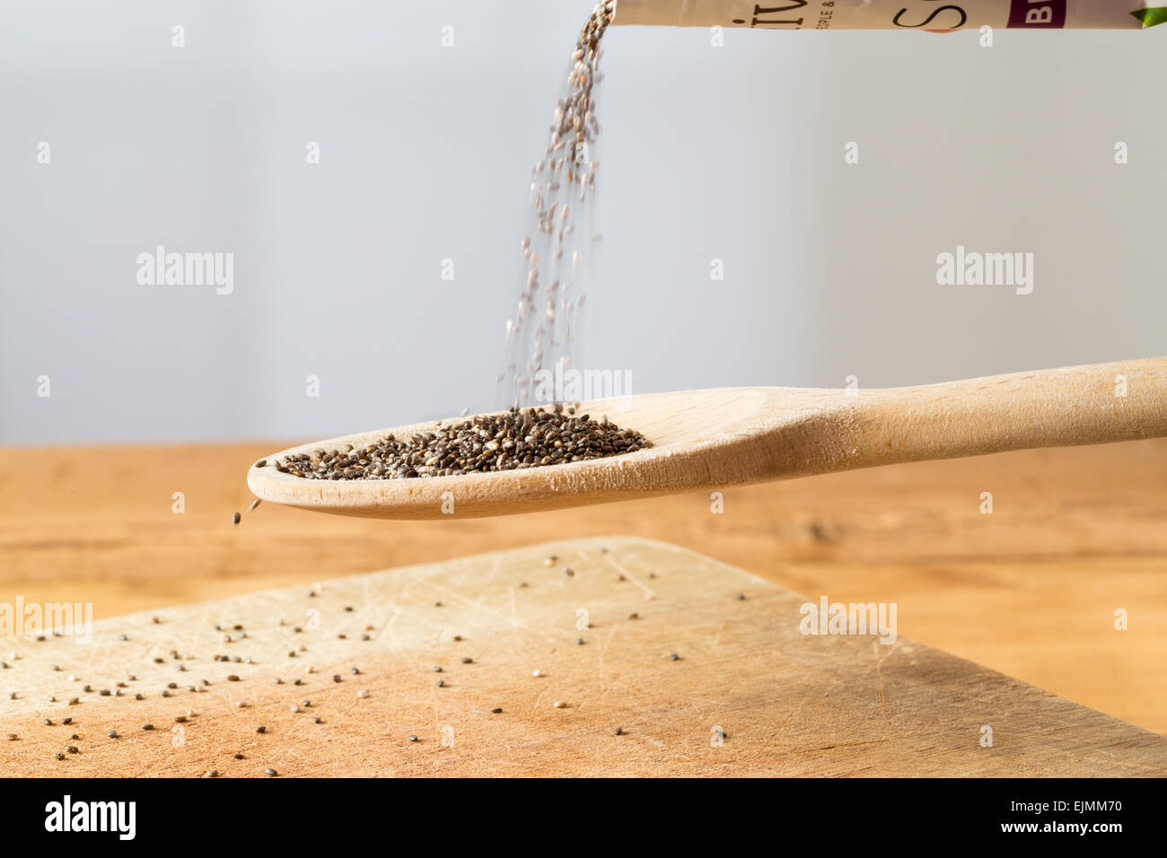 Super noto come nero semi di chia sono versata in un supporto di legno cucchiaio su legno scheda di pane sul tavolo da cucina Foto Stock