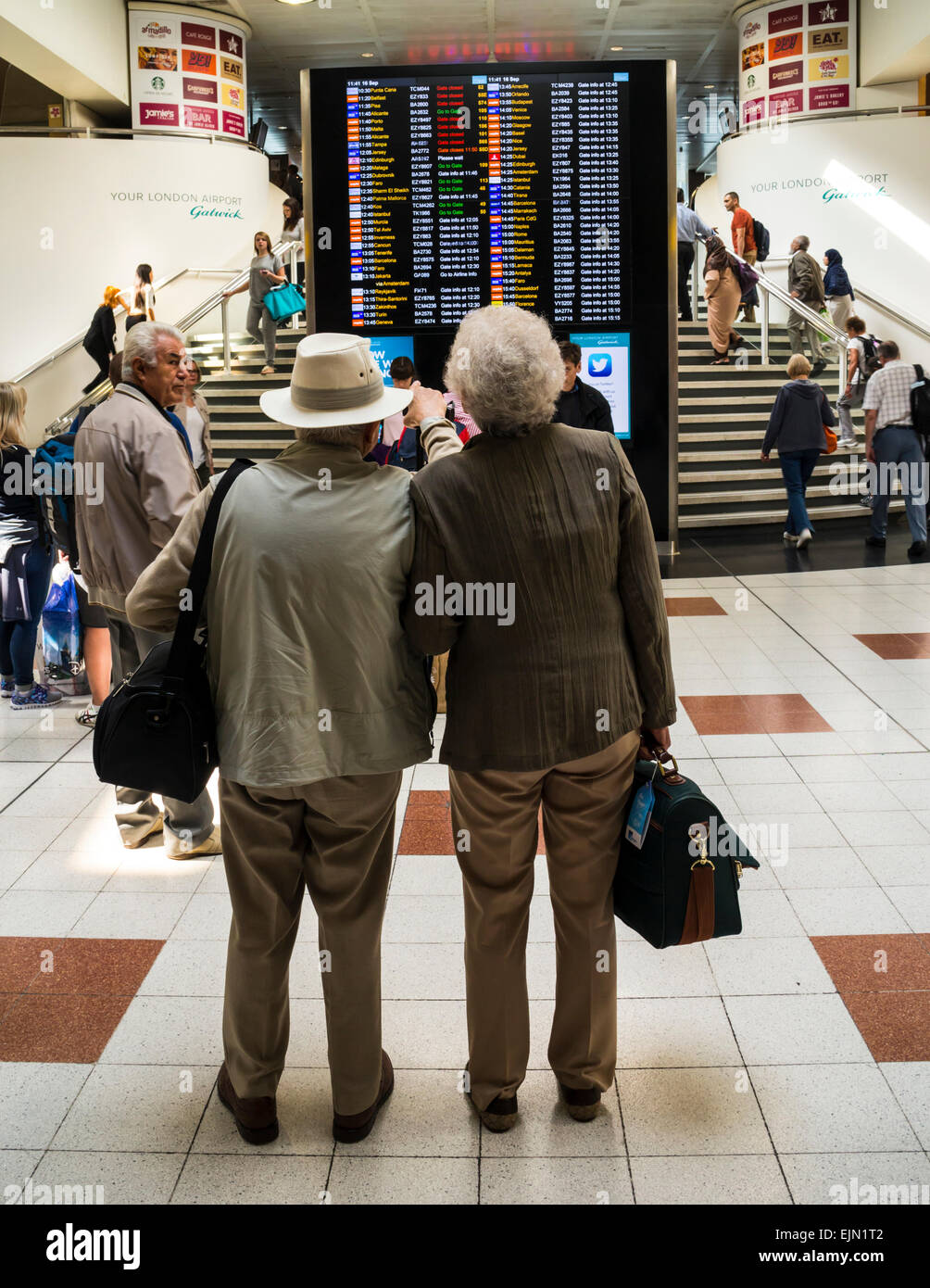 Coppia senior controllando la scheda di volo all'Aeroporto di Gatwick, terminal nord, West Sussex, in Inghilterra. Foto Stock