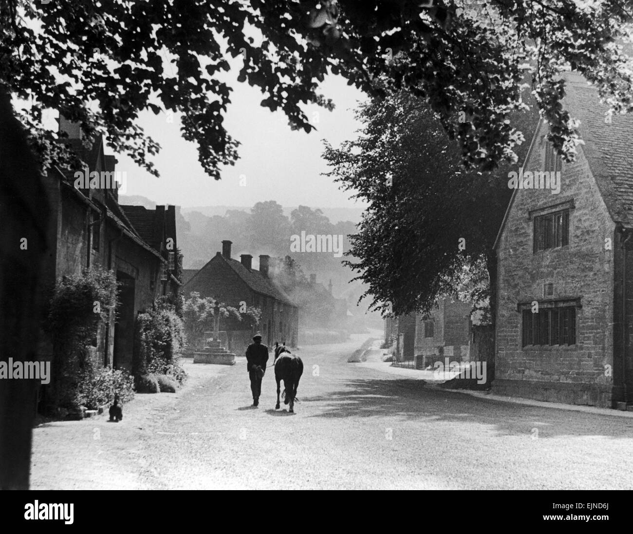 Un uomo a piedi lungo una strada di campagna con il suo pony in Stanton, un tipico villaggio Costwold. Circa 1935. Foto Stock