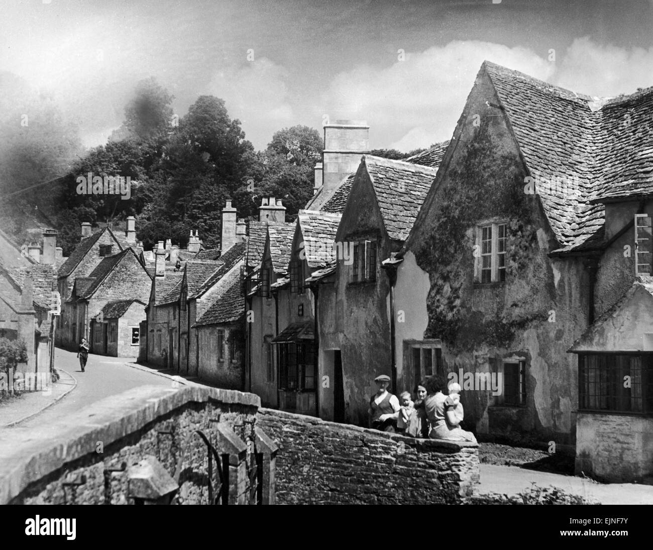 Una famiglia prende un riposo su un muro di pietra in un villaggio Costwold nel Gloucestershire. Circa 1935. Foto Stock