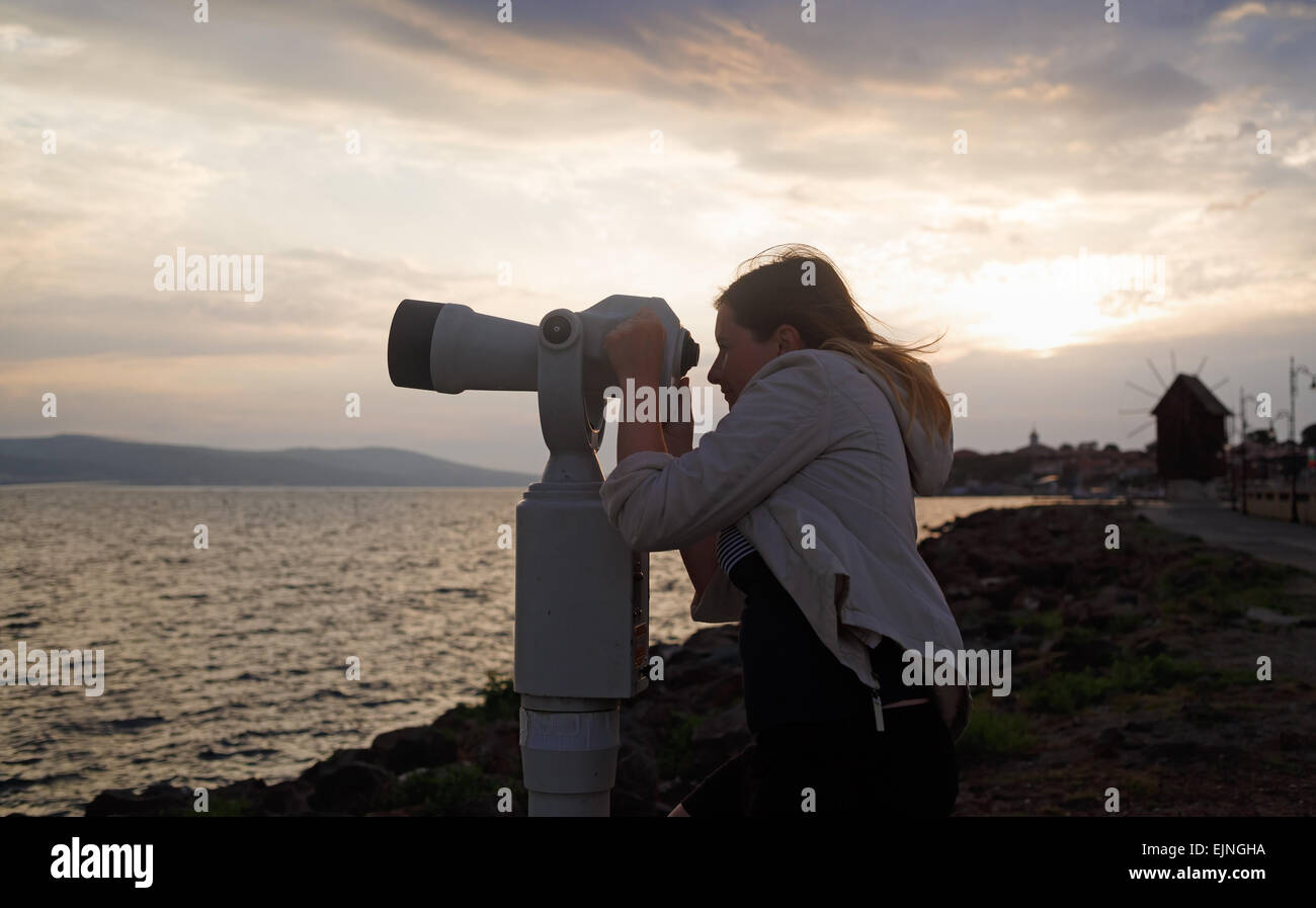 Una donna con il mare lavoro binoculare con monete sullo sfondo di un paesaggio di mare al mattino presto. Sunrise in ba Foto Stock