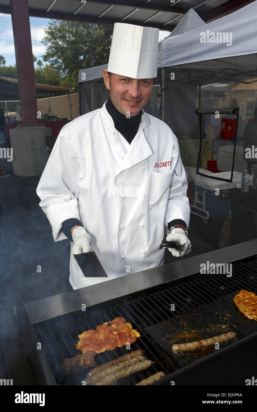 Lo Chef tendendo un barbecue vestita di bianco vestiti chef sorridente in telecamera Foto Stock