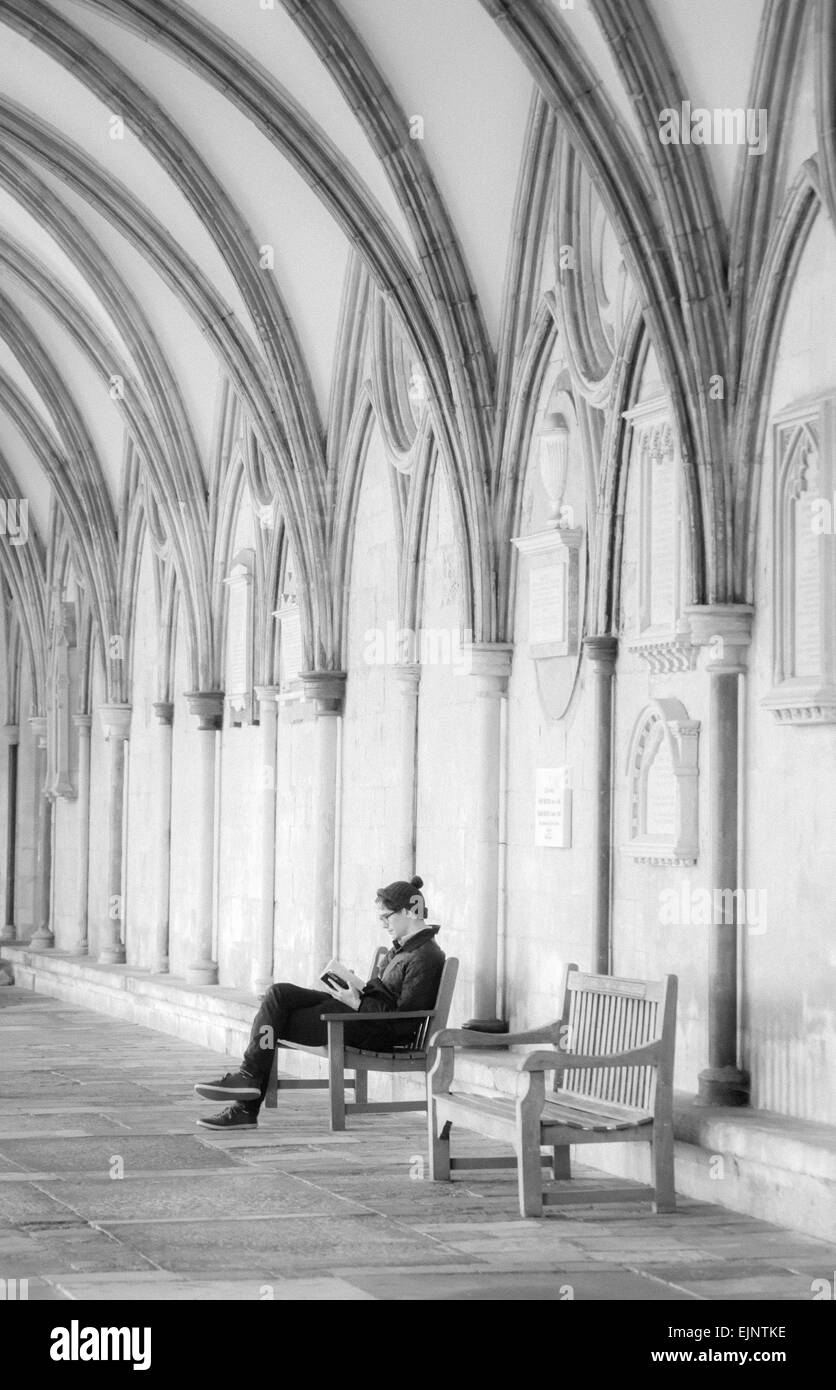 Uomo seduto su un banco di lavoro per leggere un libro nella quiete dei chiostri presso la Cattedrale di Salisbury, Salisbury, Wiltshire, Regno Unito in Marzo Foto Stock