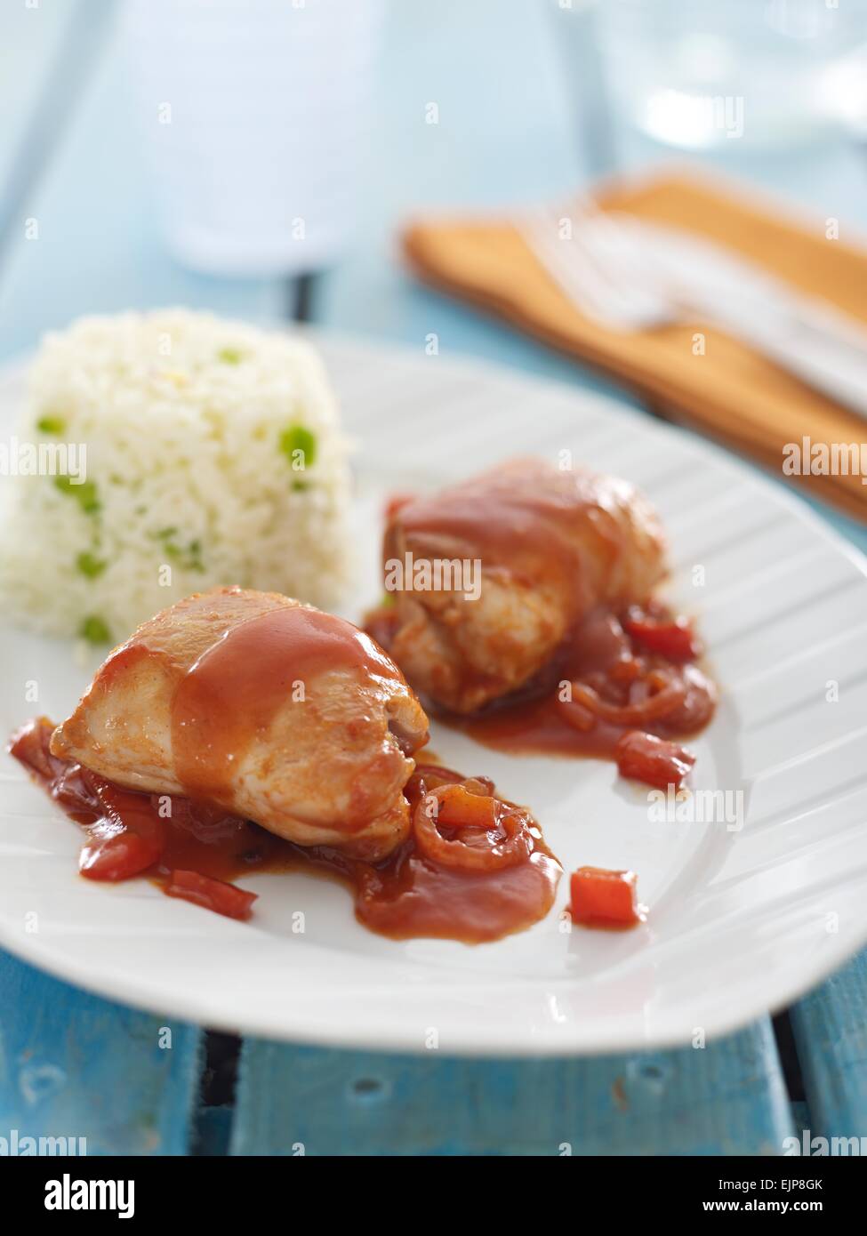 Cosce di pollo in un pomodoro e salsa di cipolle servito con una torre di riso su una rustica blu lavato a doghe di tavolo in legno Foto Stock