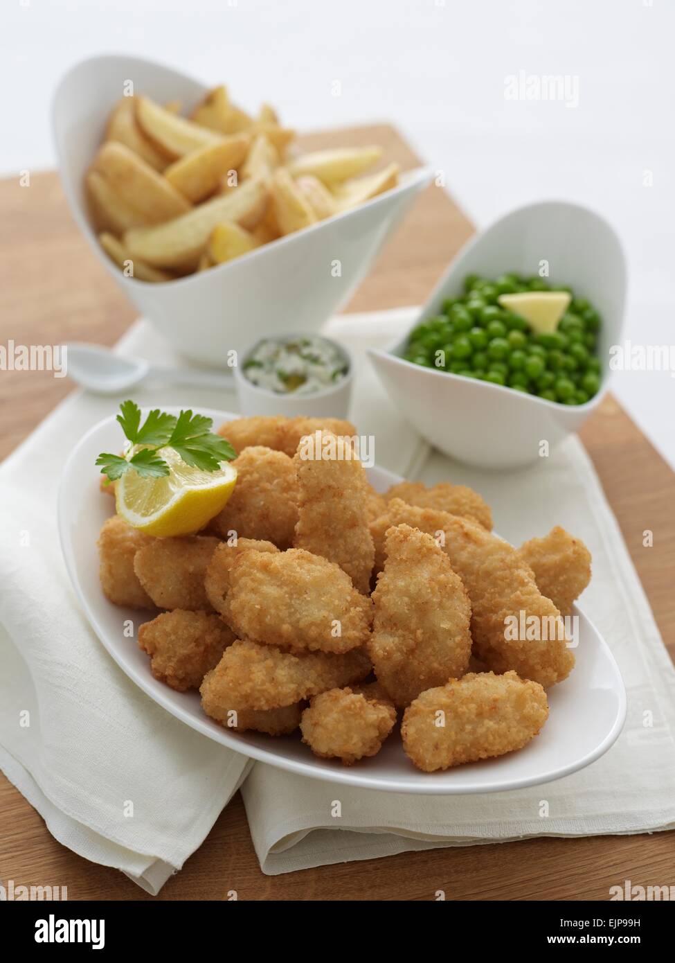 Pesce impanati pepite trucioli e piselli in recipienti separati, tavola di legno Foto Stock
