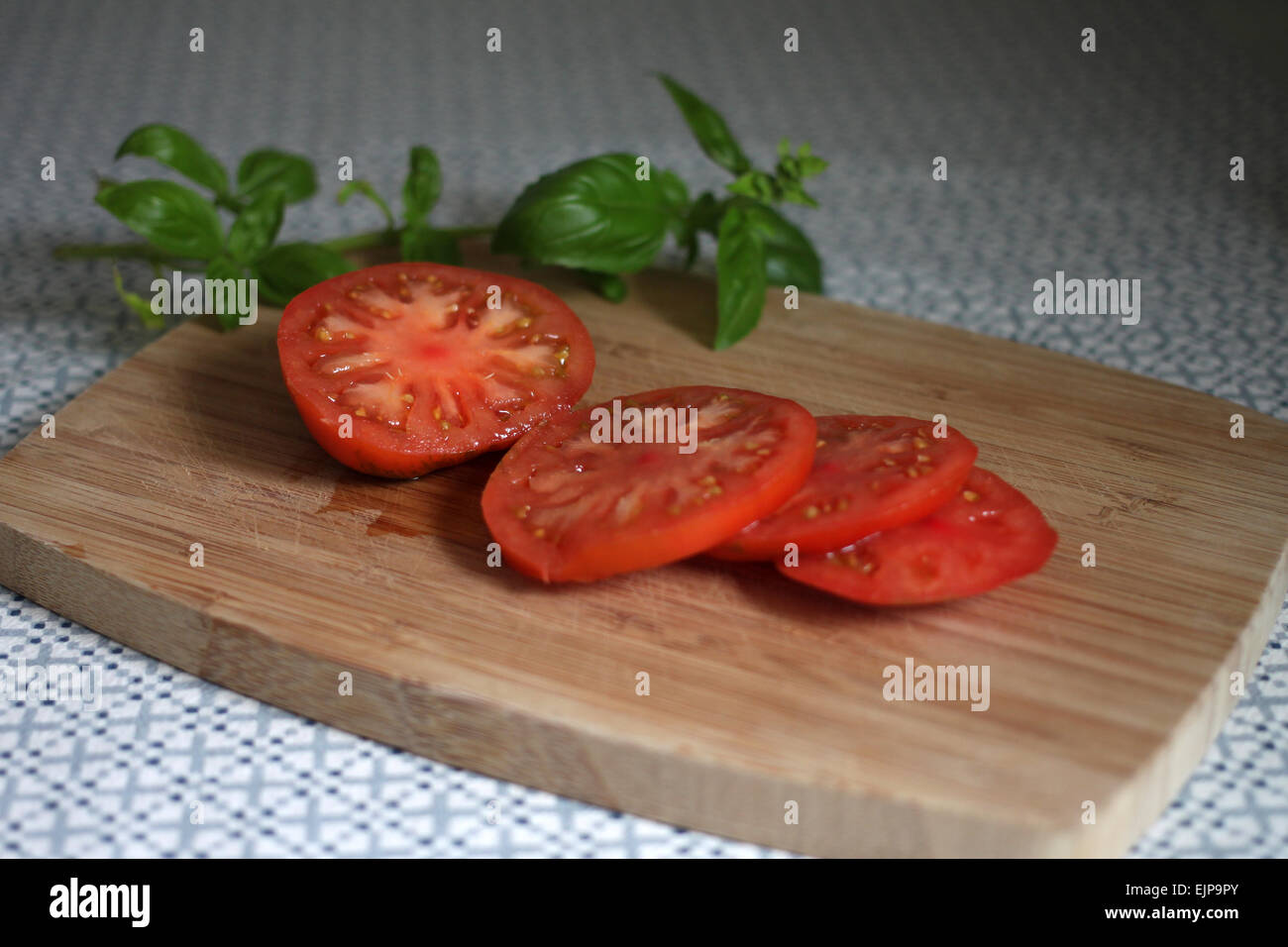 Raf (pomodoro Solanum lycopersicum) e le foglie di basilico sul tagliere di legno sul panno della tabella Foto Stock