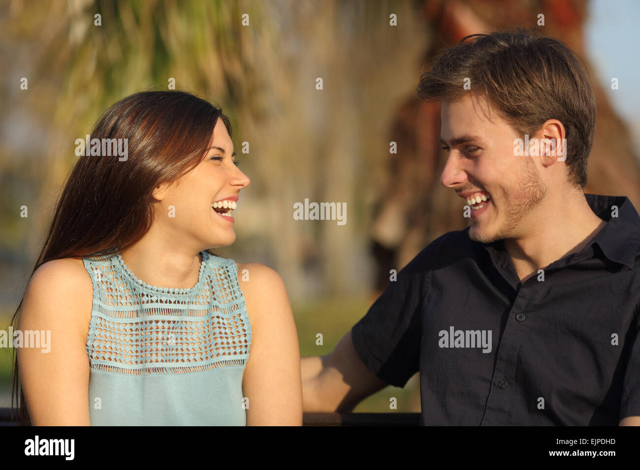 Amici o coppia di ridere e tenuto una conversazione seduta su una panchina nel parco Foto Stock