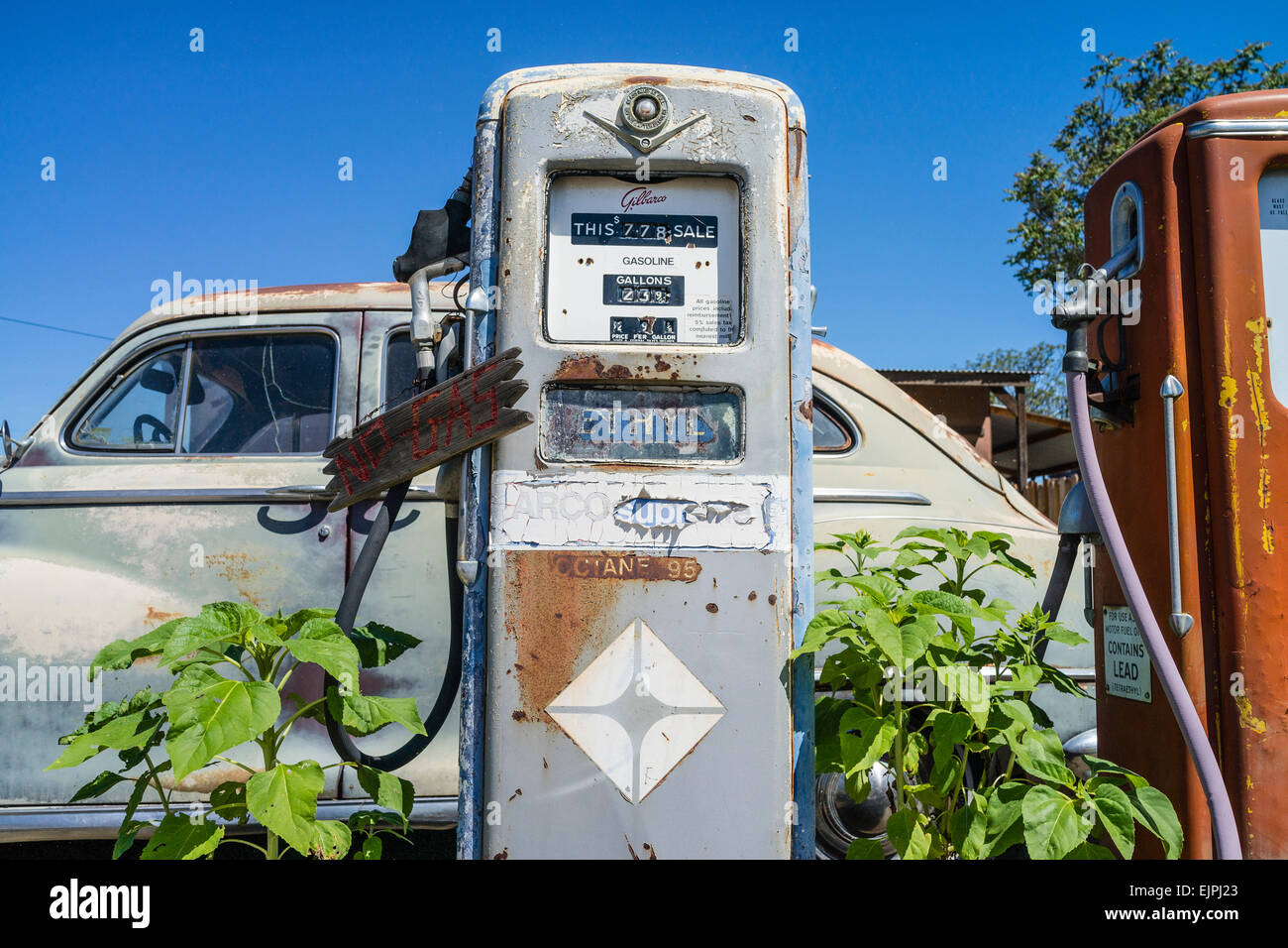 Un 1947 Chrysler berlina 4 porte la formazione di ruggine con vernice sbiadita siede parcheggiata di fronte due vecchio stile pompe di gas in corrispondenza di una stazione di riempimento. Foto Stock