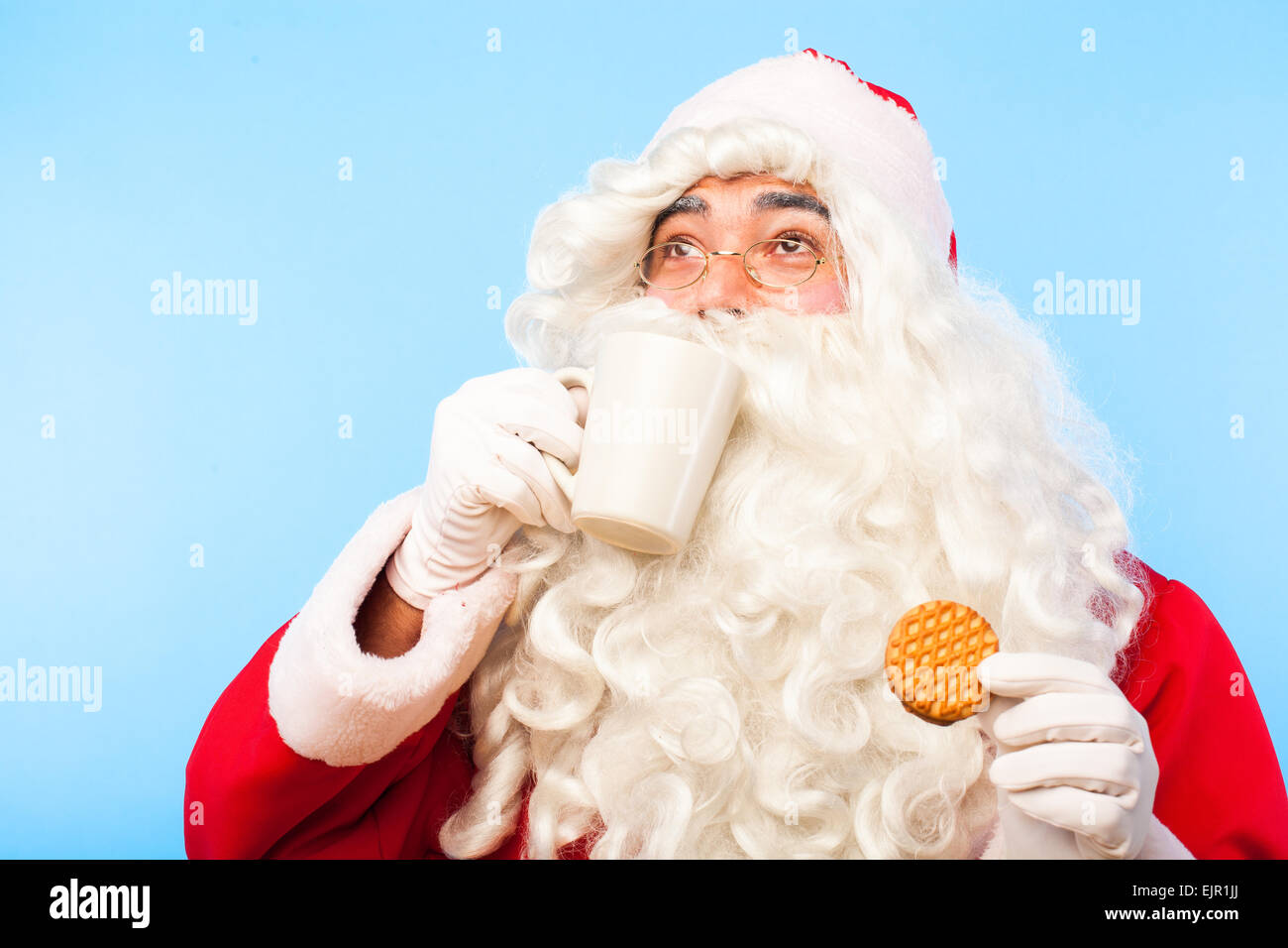 Babbo Natale bevendo un bicchiere di latte con un biscotto in mano, guardando in alto Foto Stock