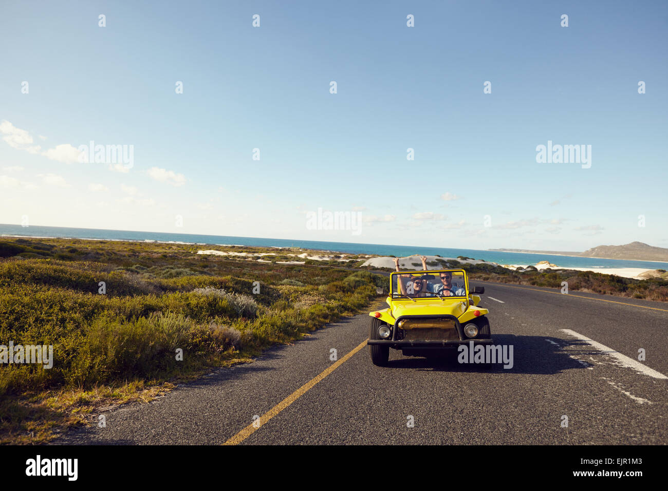 Coppia giovane guida lungo una strada aperta entusiasta di essere su un roadtrip. Coppia felice alla guida di una vettura con le braccia alzate. Foto Stock