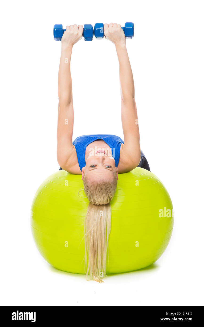 Donna bionda indossando indumenti fitness esercizio con pesi su una sfera di colore giallo Foto Stock