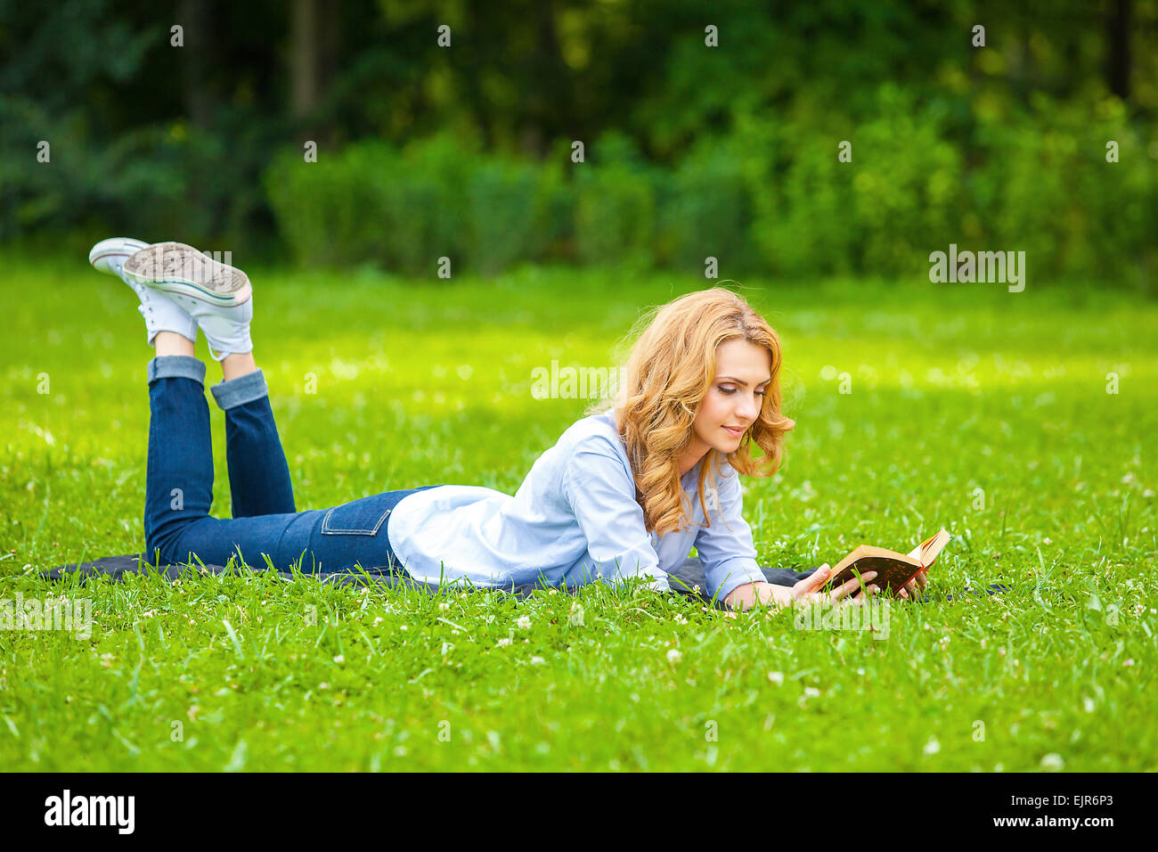 Bella donna bionda giacente in erba e la lettura di un libro Foto Stock