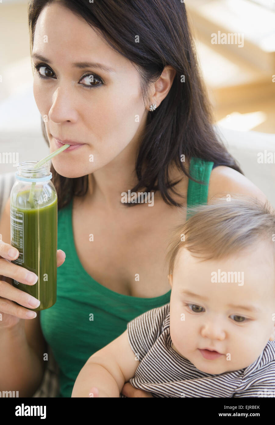 Close up di razza mista azienda madre e bambino bere il succo verde Foto Stock