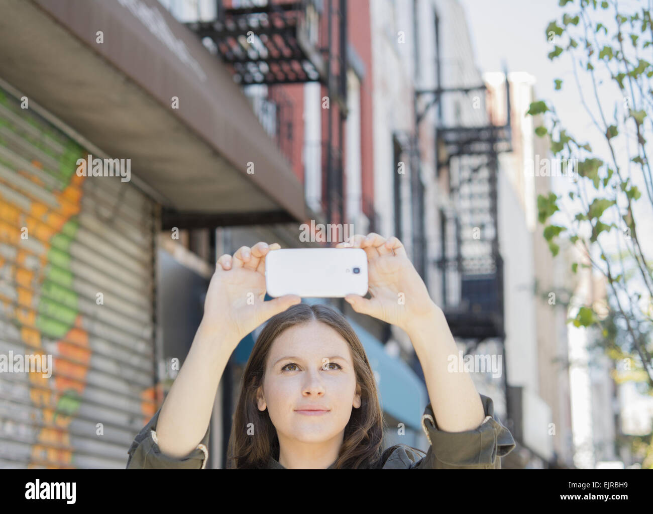 La donna caucasica tenendo il telefono cellulare la fotografia sul marciapiede urbano Foto Stock