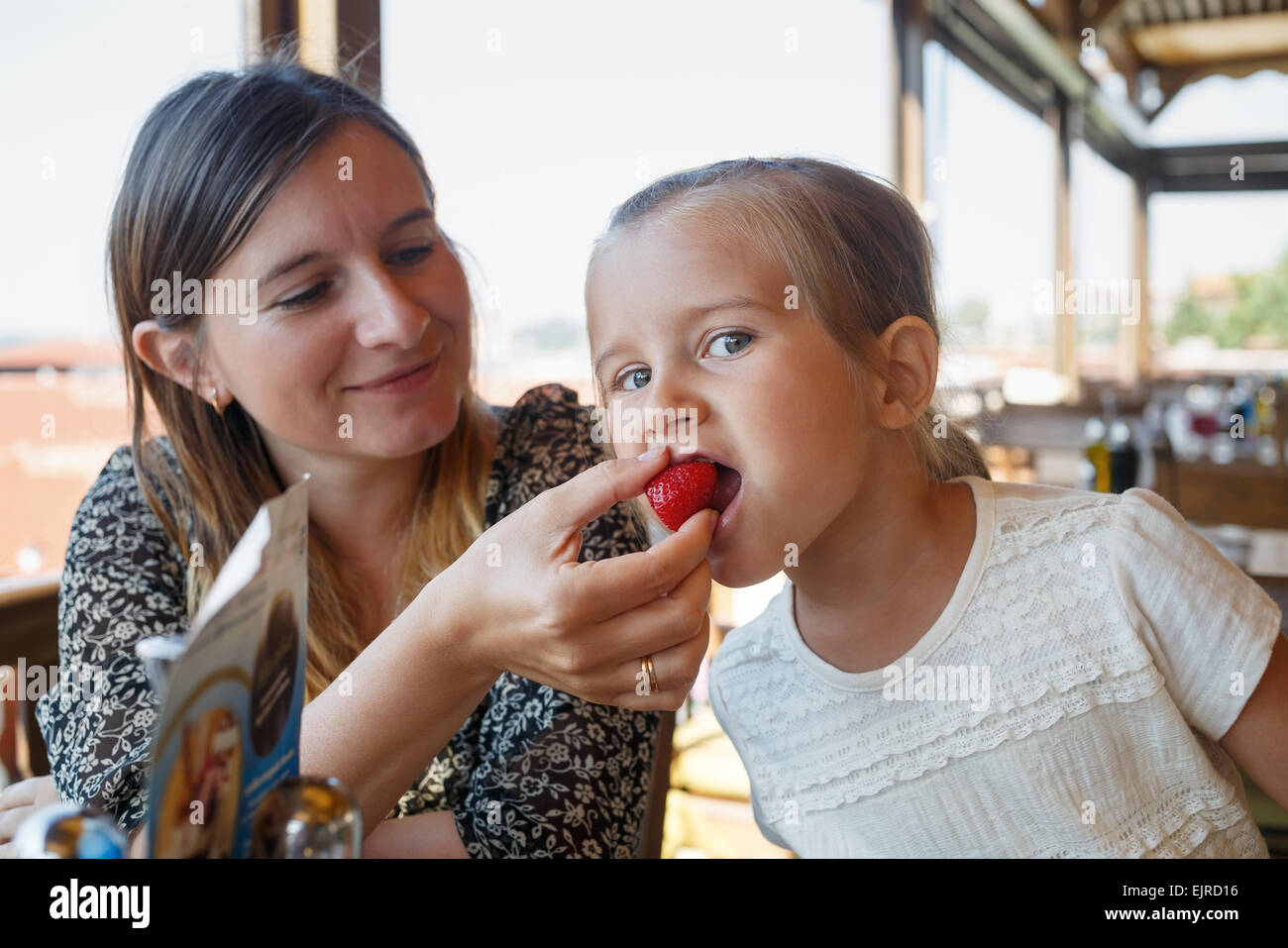 Mamma alimenta il bambino delizioso dolce fragole nel ristorante. Profondità di campo. Focus sul bambino del viso. Foto Stock