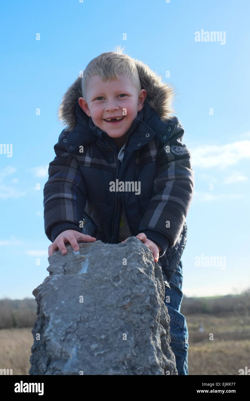Sorridente ragazzo di età compresa tra i sei senza denti frontali giocando sulla roccia al di fuori di aria fresca. Foto Stock