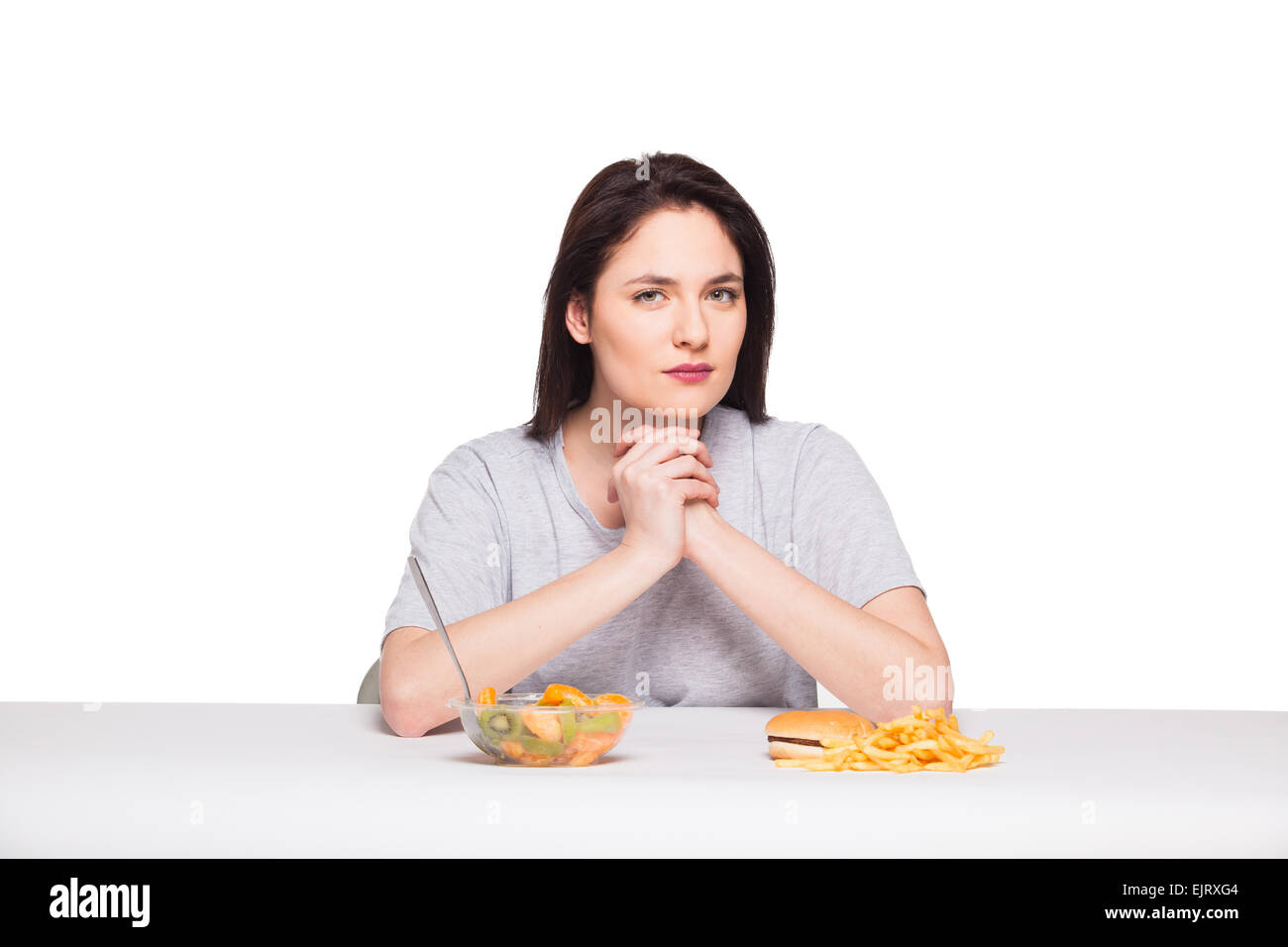 Immagine di donna con frutta e hamburger davanti a pensare a scelta su sfondo bianco, sano versus junk food concept Foto Stock