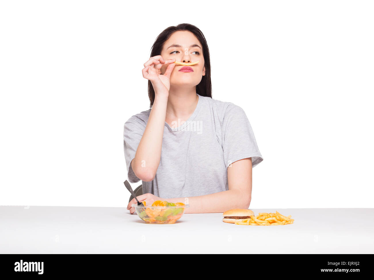 Naturale donna espressiva giocando con patatine fritte, avendo di fronte junk e cibo sano, isolato su bianco Foto Stock