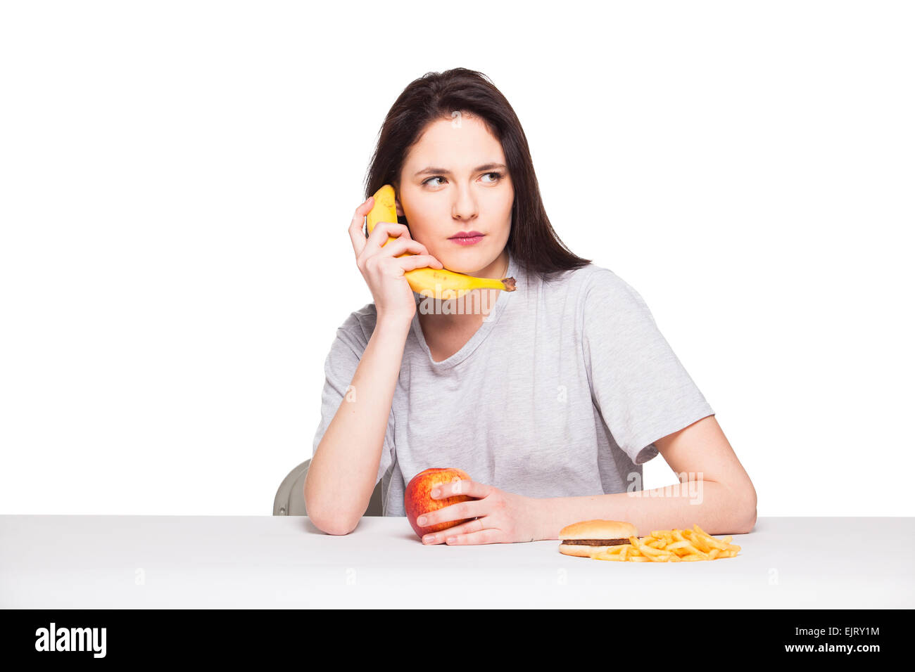 Naturale donna espressiva giocando con frutti, avendo di fronte junk e cibo sano, isolato su bianco Foto Stock