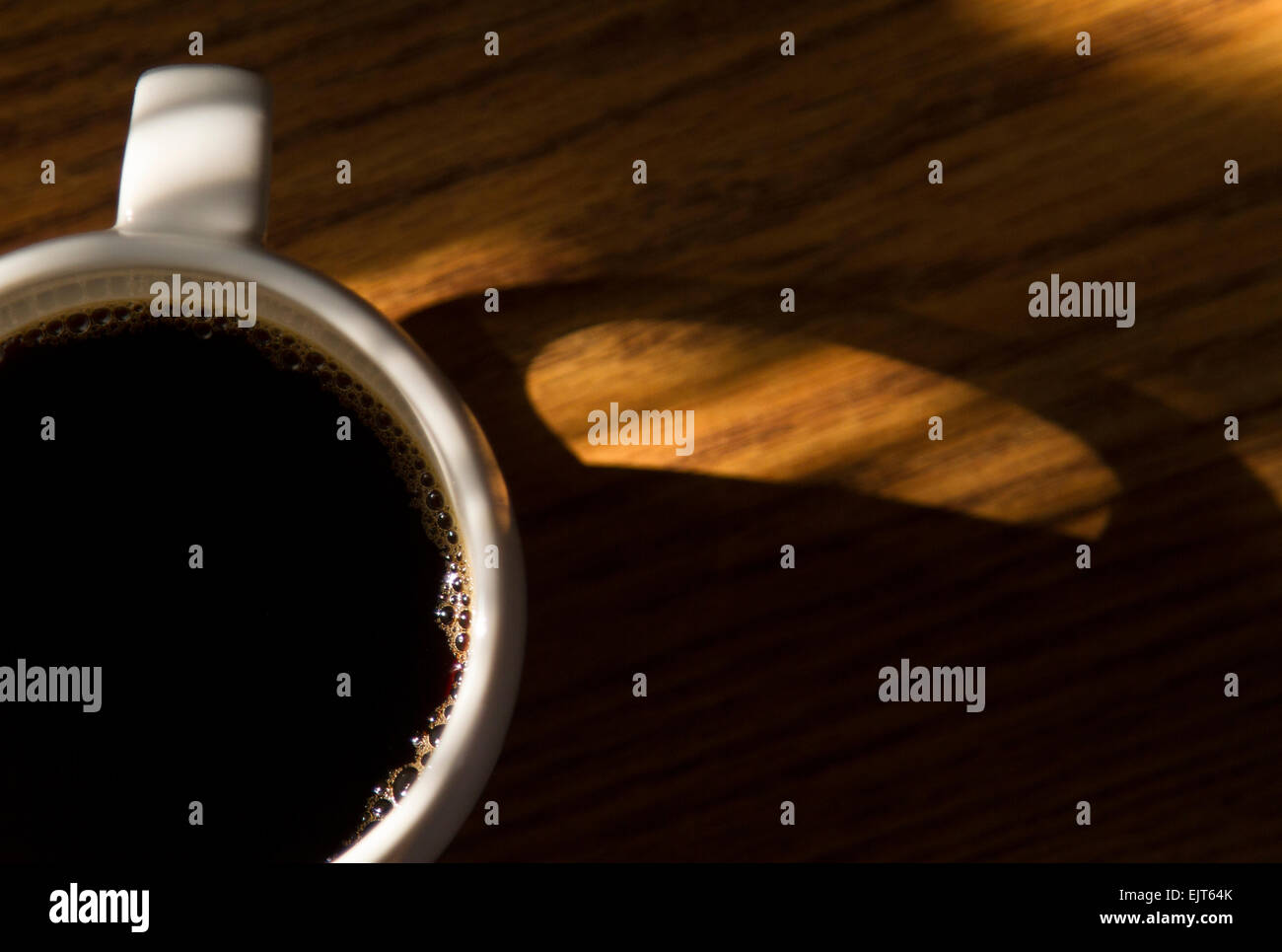 Una nuova tazza di caffè si siede su una scrivania in sole mattutino. Foto Stock