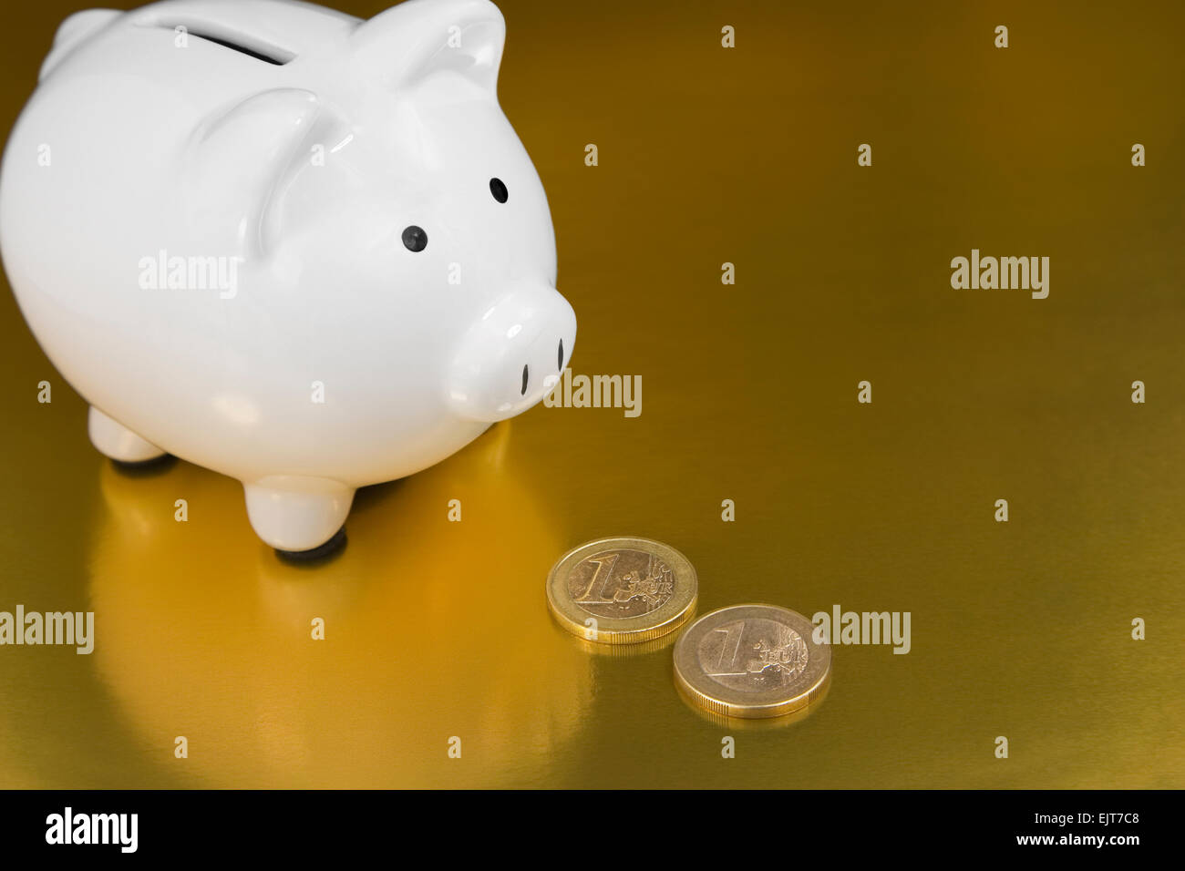 White salvadanaio con un conio di monete metalliche in euro su un fondo dorato Foto Stock