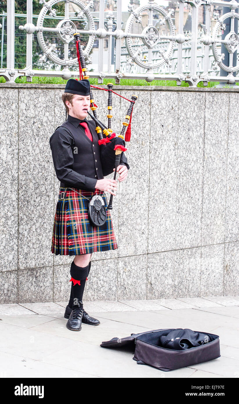 Un giovane bagpiper indossando un tradizionale rosso plaid kilt svolge per le donazioni per le strade di Edimburgo, in Scozia. Foto Stock