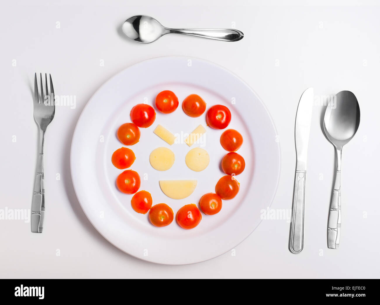 Ridendo emoticon cibo, realizzata dal formaggio e pomodori, su una piastra con posate, isolato Foto Stock