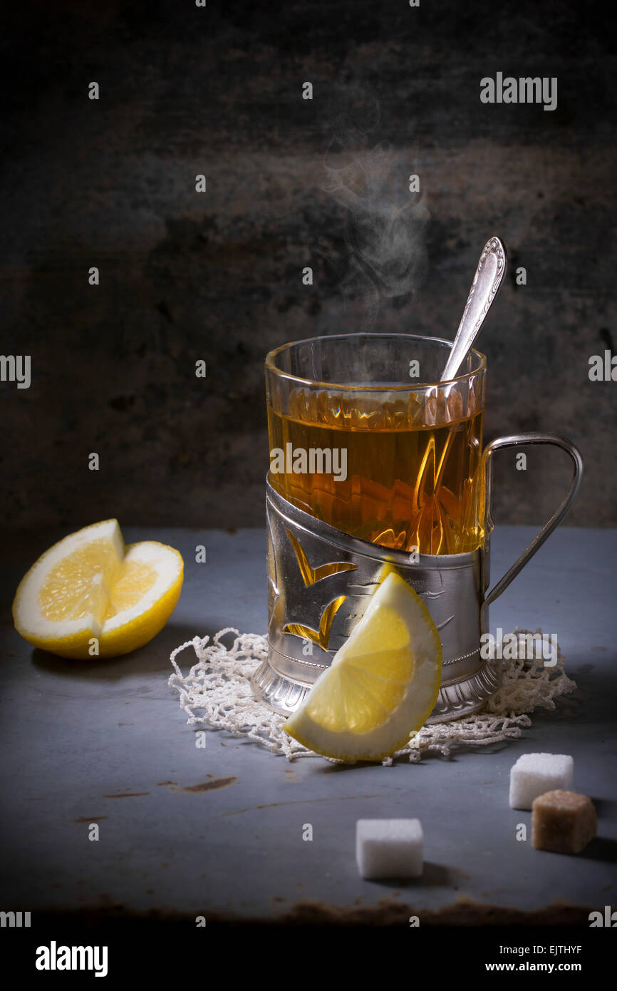 Vintage portabicchiere sul tovagliolo di maglia con la tazza di tè con fette di limone e cubetti di zucchero sopra il vecchio tavolo in metallo. Foto Stock