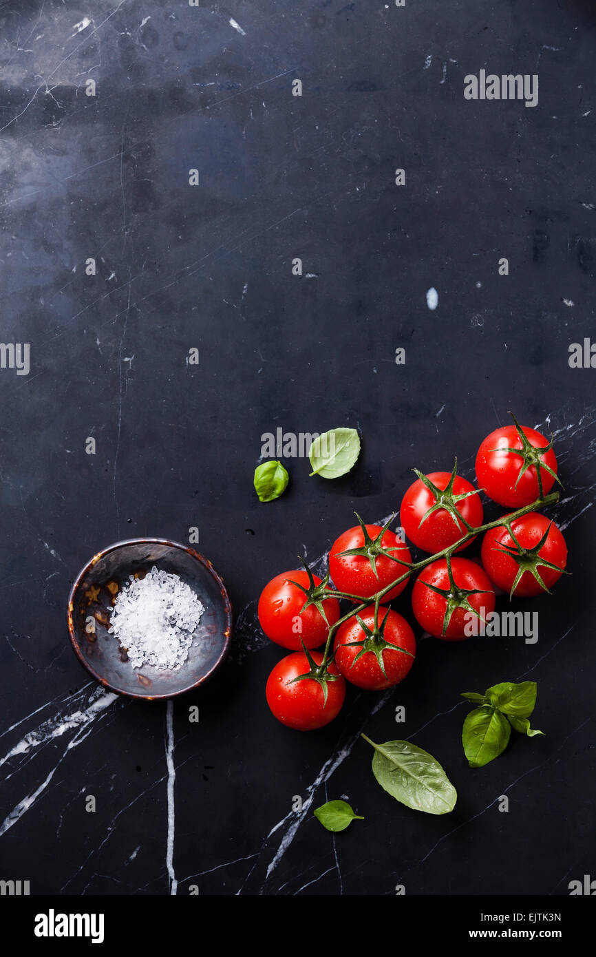 Pomodori ciliegia e il verde del basilico foglie scure su Sfondo marmo Foto Stock