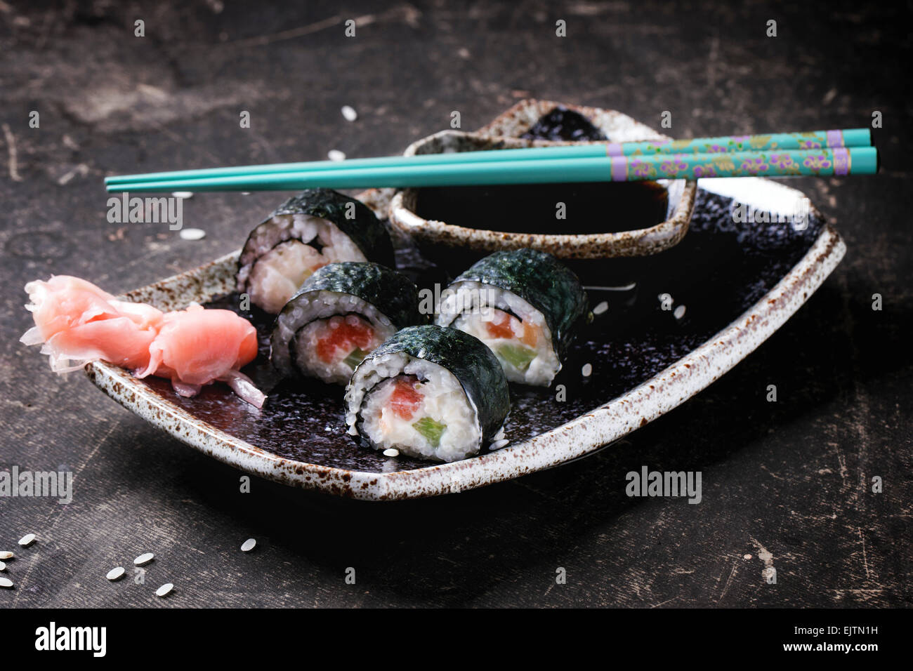 Rotoli di Sushi con salmone, servita su piastra nera con zenzero sott'aceto, la salsa di soia e il turchese bacchette su sfondo scuro. Foto Stock