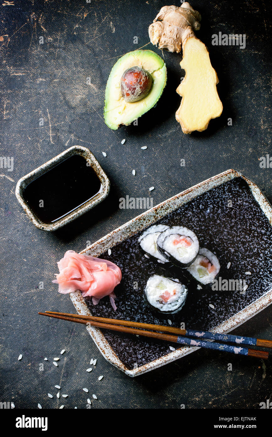 Rotoli di Sushi con salmone, servita su piastra nera con zenzero sott'aceto, avocado e salsa di soia e bastoncini su sfondo scuro. T Foto Stock