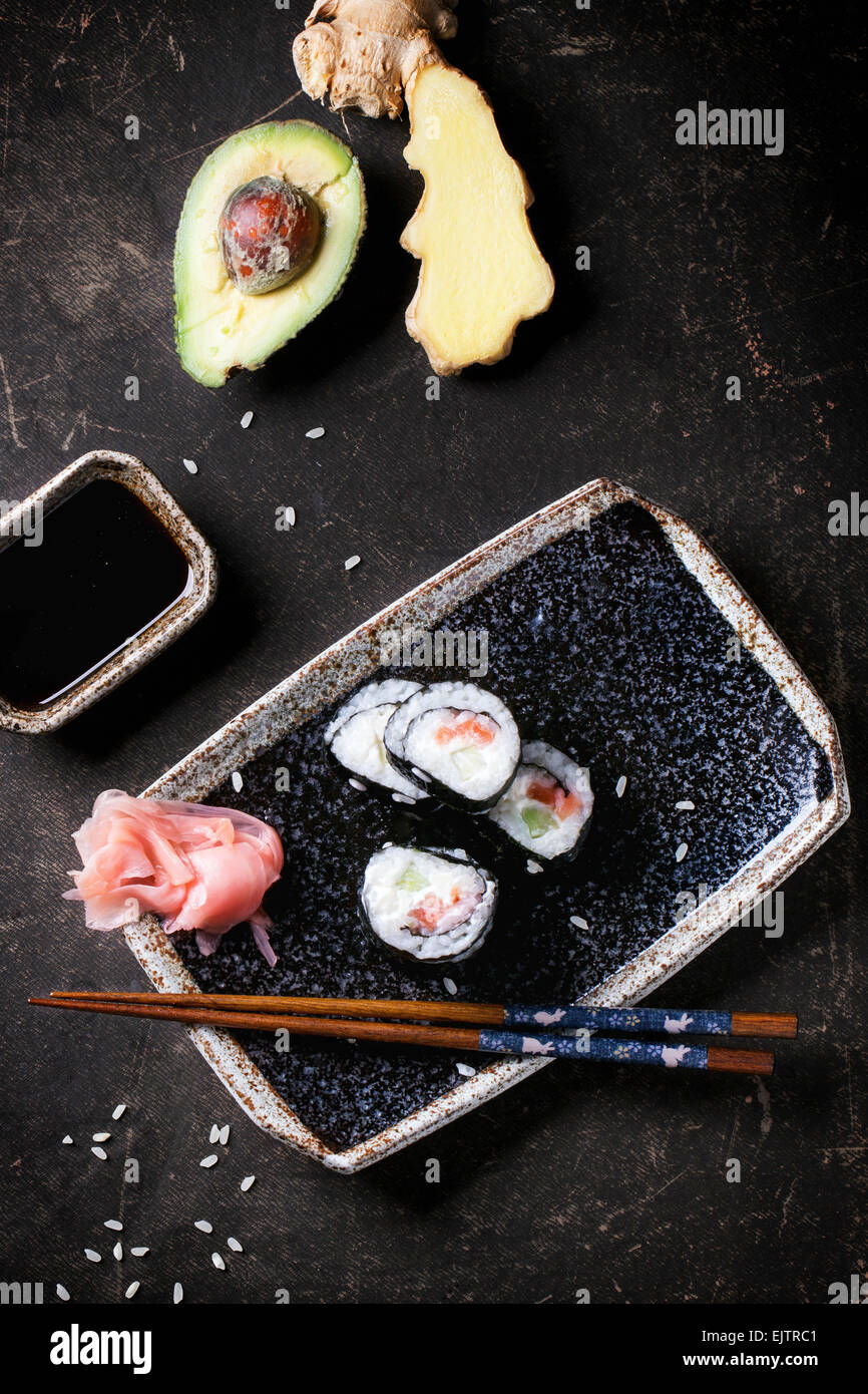 Rotoli di Sushi con salmone, servita su piastra nera con zenzero sott'aceto, avocado e salsa di soia e bastoncini su sfondo scuro. T Foto Stock