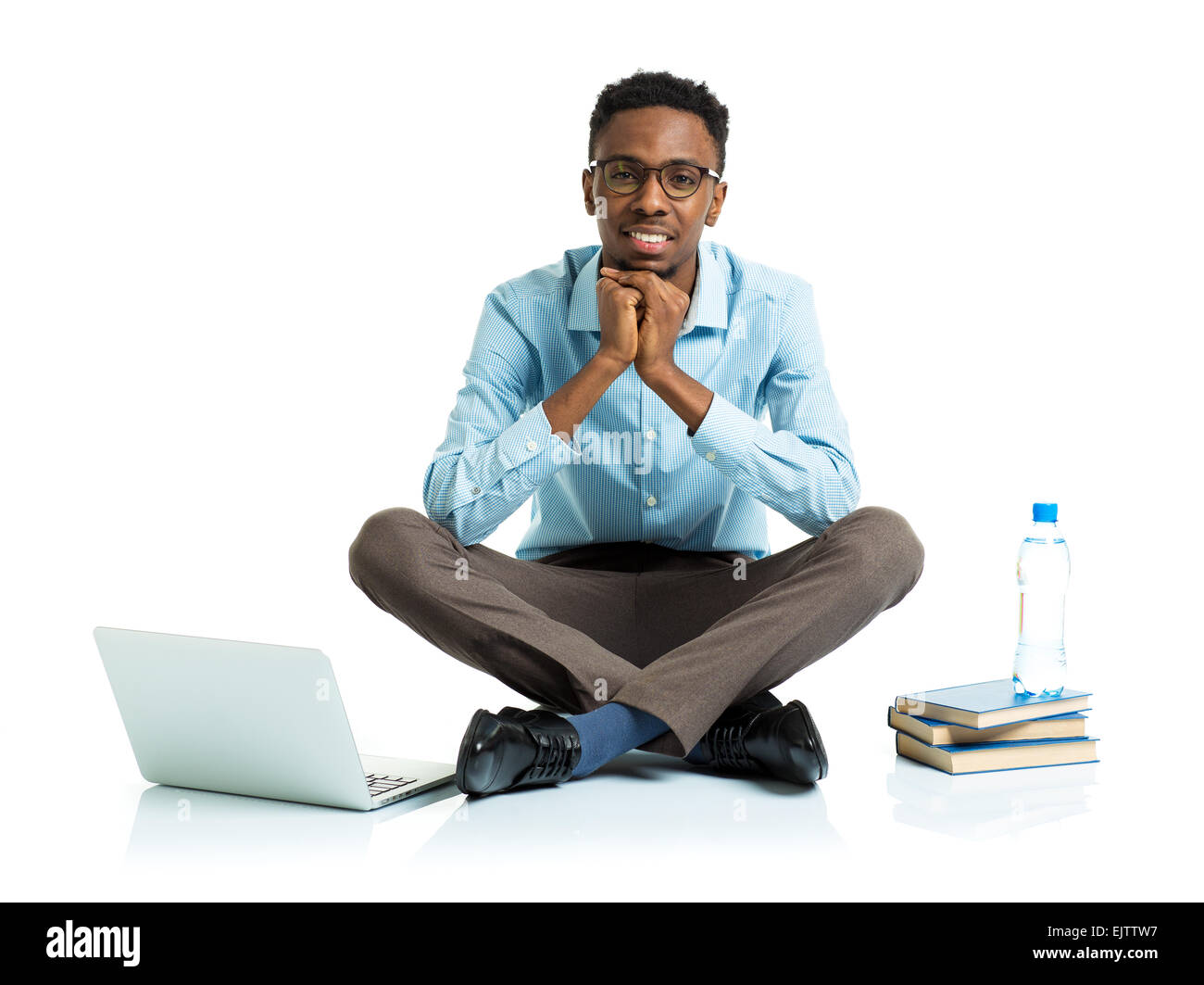 Felice americano africano studente di college con il computer portatile, libri e una bottiglia di acqua seduto su sfondo bianco Foto Stock