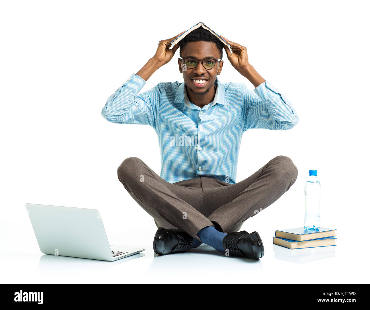 Felice African American college studente seduto con laptop e un libro sul suo capo su sfondo bianco Foto Stock