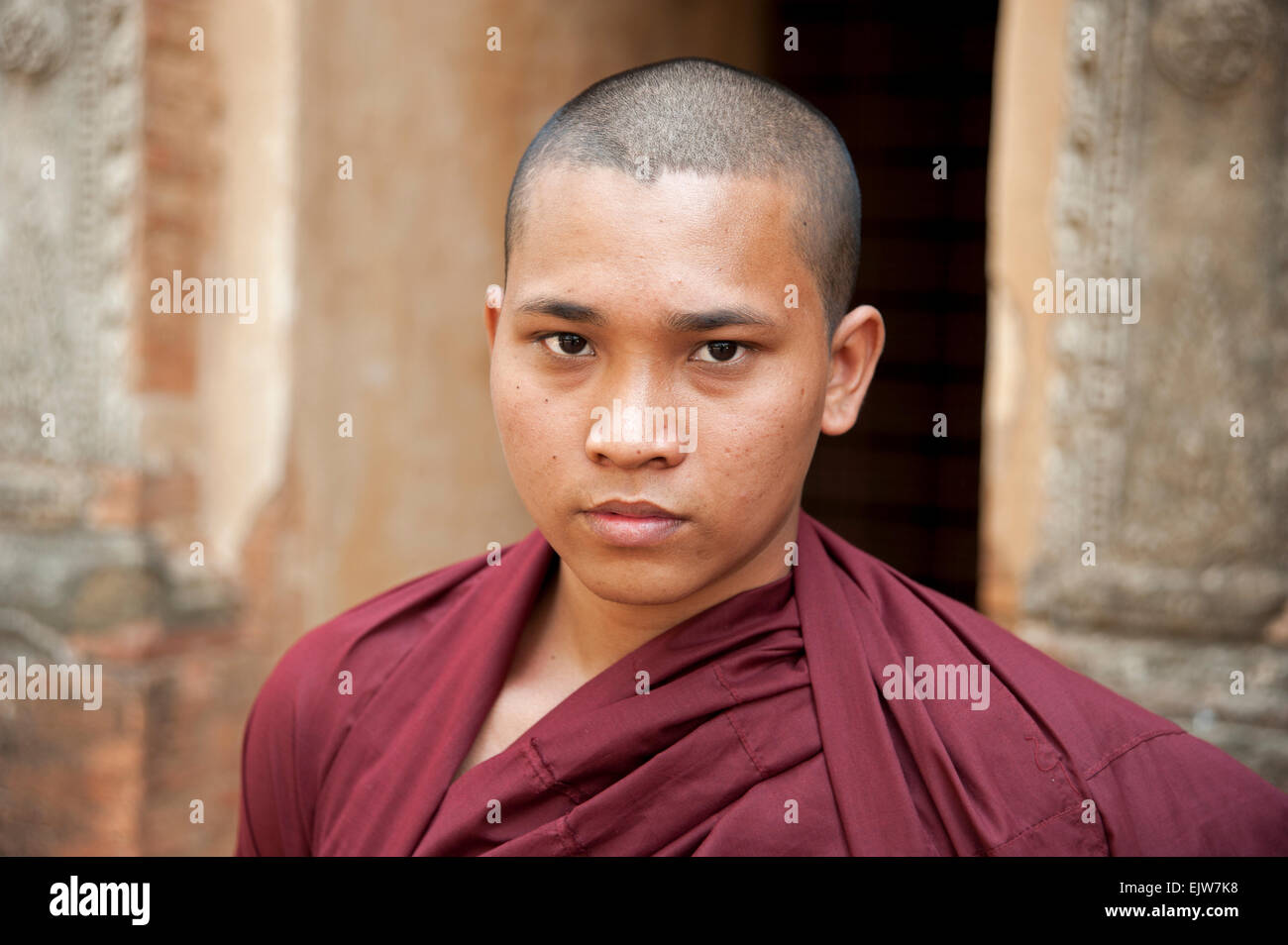 Ritratto di un monaco buddista che indossa vesti rosse contro il muro di pietra e ingresso di un tempio di Bagan MYANMAR Birmania Foto Stock