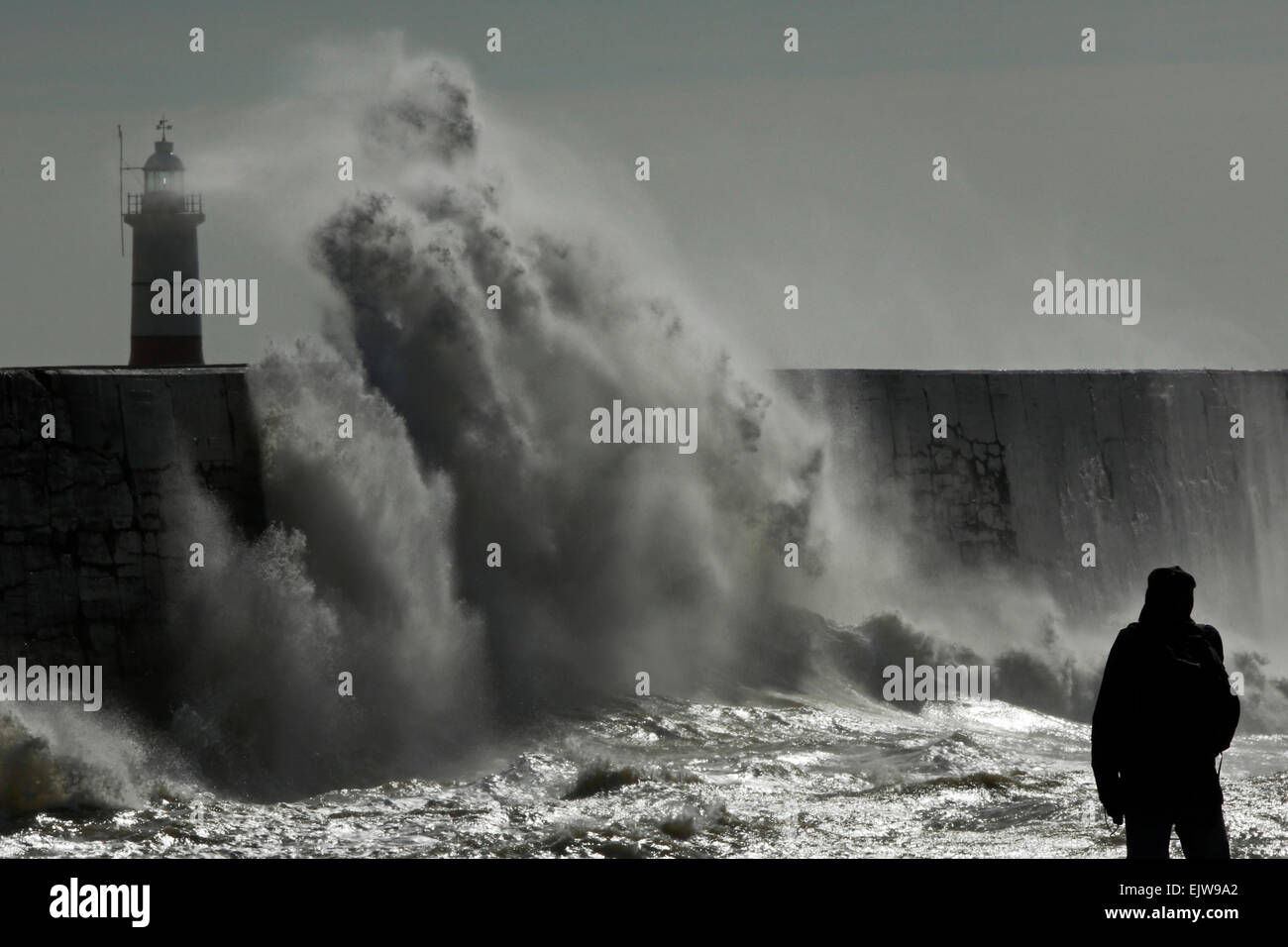 Un uomo orologi come onde infrangersi contro la parete del porto a Newhaven in East Sussex, Regno Unito Foto Stock