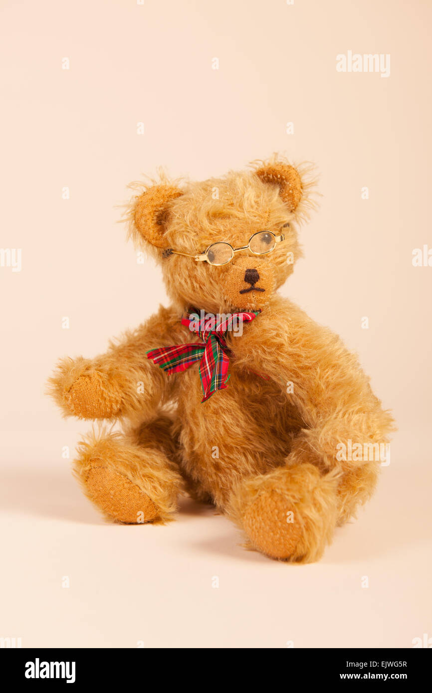 Farcite orso vintage con gli occhiali seduto su sfondo beige Foto Stock