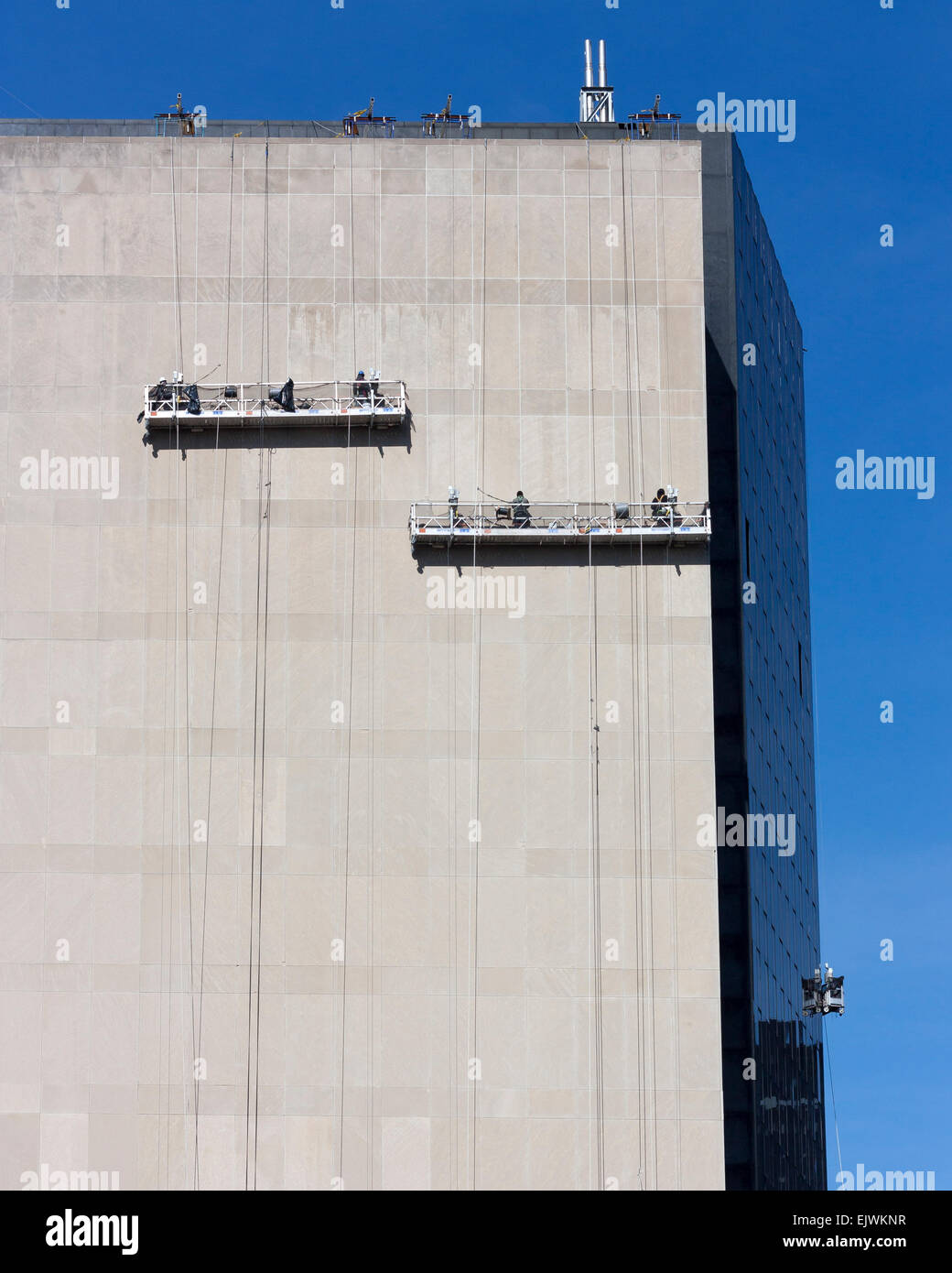 Lavoratori in piattaforma sospesa lavorando sul lato senza finestre di un grattacielo a New York City. Foto Stock