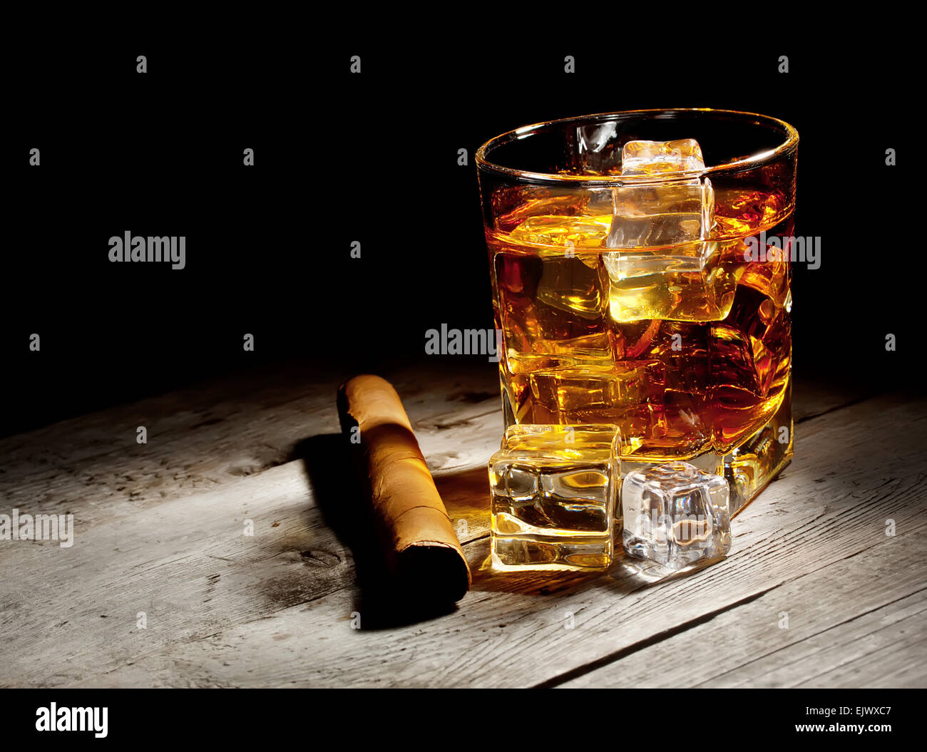 Bicchiere di whiskey invecchiati con sigaro e cubetti di ghiaccio sul tavolo di legno Foto Stock