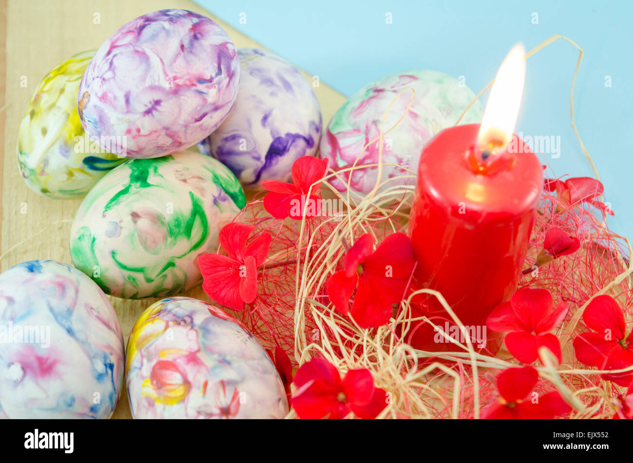Dozzina di colorate a mano le uova di Pasqua e un rosso candela che brucia decorate con fiori di colore rosso e nastri Foto Stock