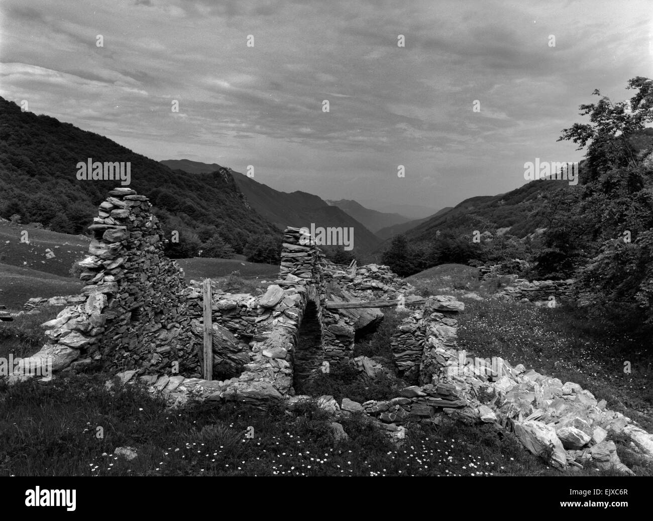 Il nero e il bianco paesaggio di rovine in primo piano e le montagne come sfondo sotto il cielo pesante. Foto Stock