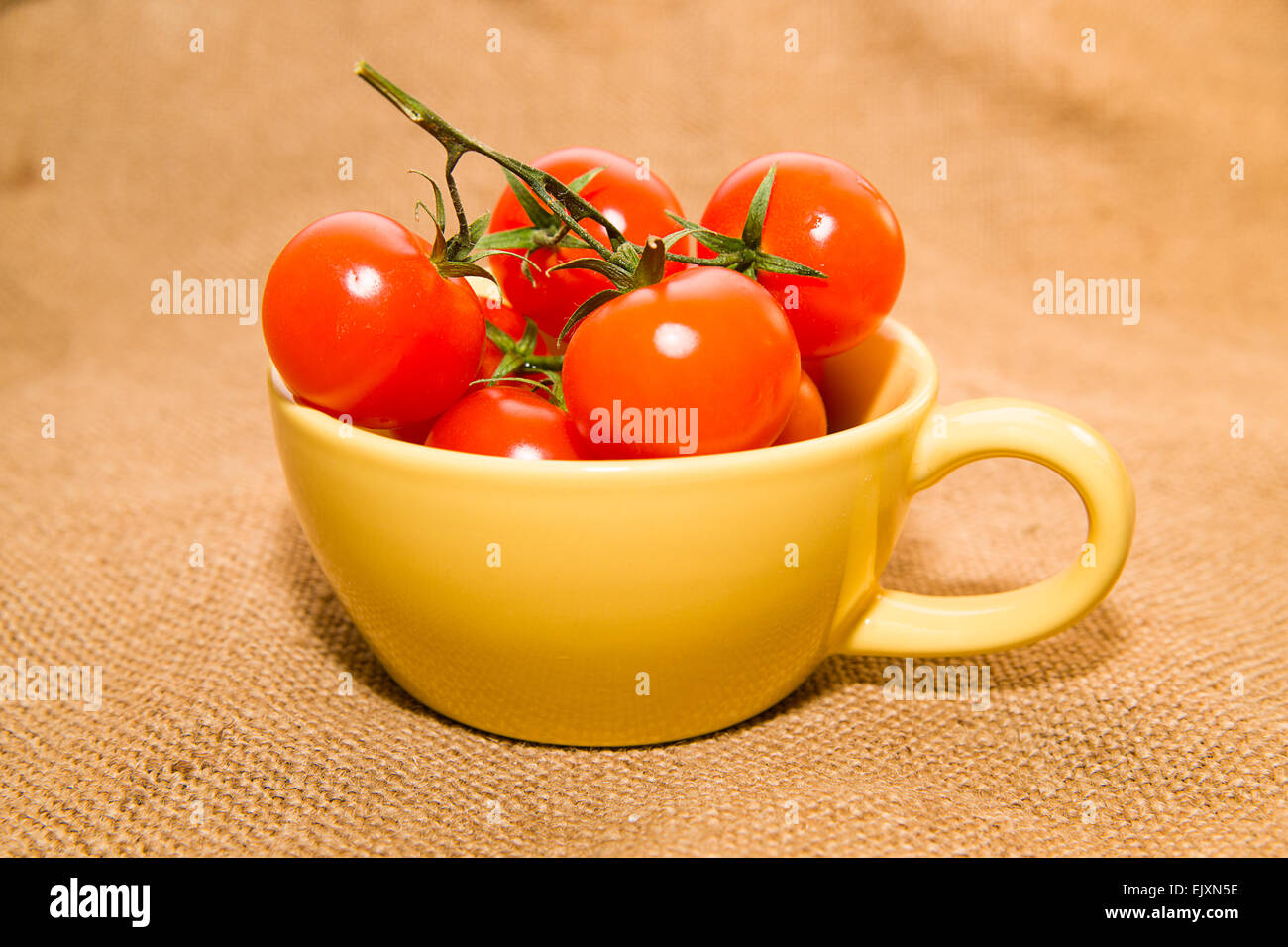 Pomodori ciliegia in una tazza di colore giallo sul panno vecchio Foto Stock