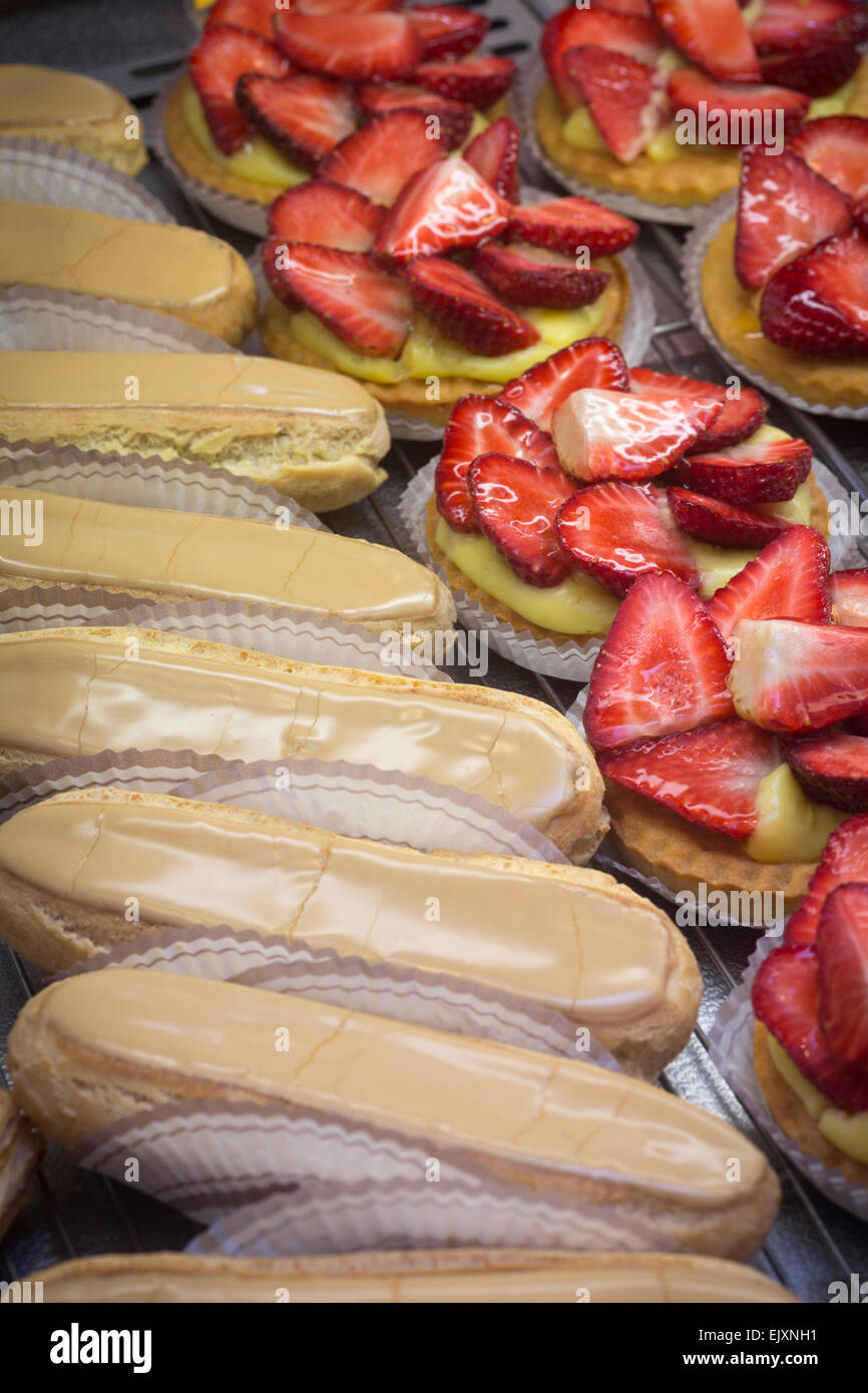 Éclairs con caffè e fragola canapes visualizzato nel negozio di dolci finestra (Francia). Éclairs au café et tartelettes aux fraises. Foto Stock