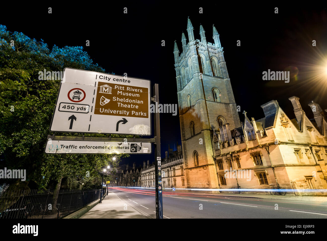 Un cartello stradale per Oxford City Centre e i punti di interesse dietro il quale è il Magdalen College di Oxford University visto durante la notte. Foto Stock