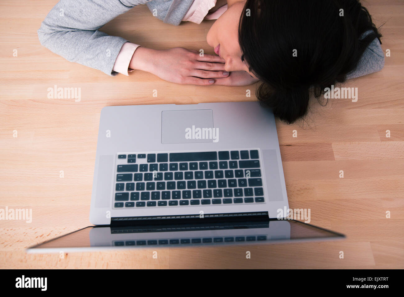 Giovane donna che dorme sul tavolo di legno con il computer portatile Foto Stock